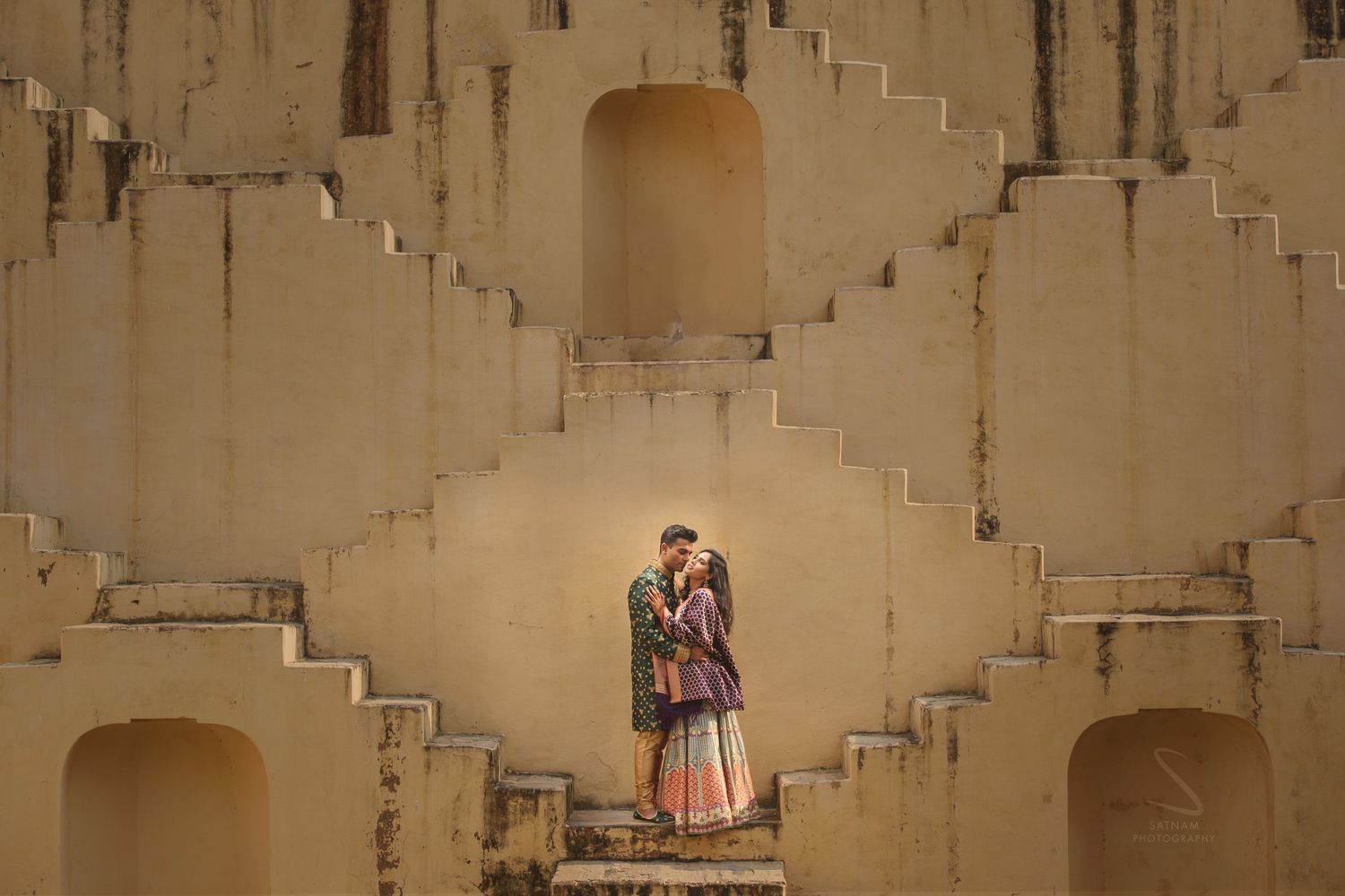 Indian couple embraces romantically in a niche of the symmetrical sandstone steps of a Jaipur stepwell.