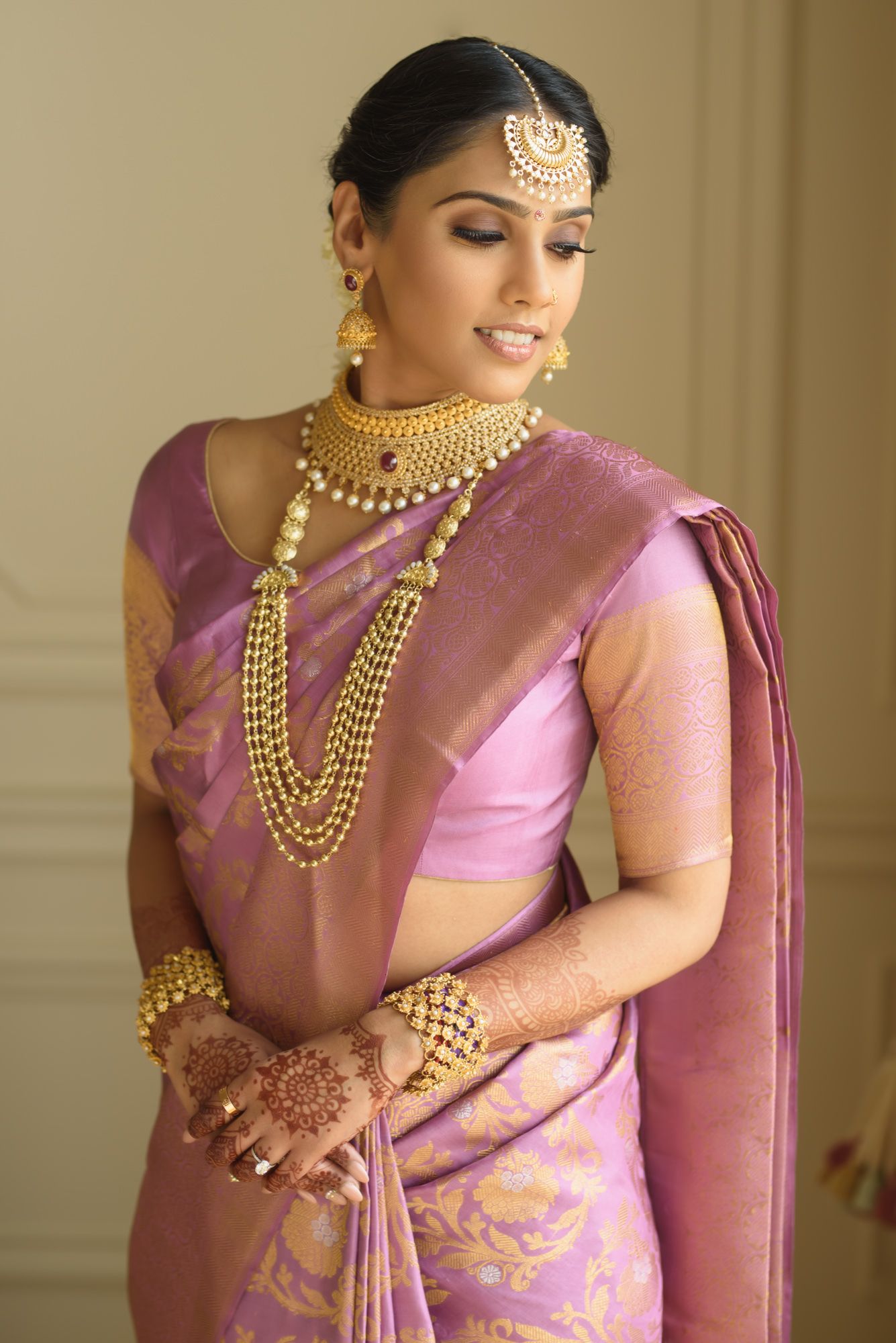 South Indian bride in purple Kanjivaram silk saree with gold jewelry and mehndi hands.
