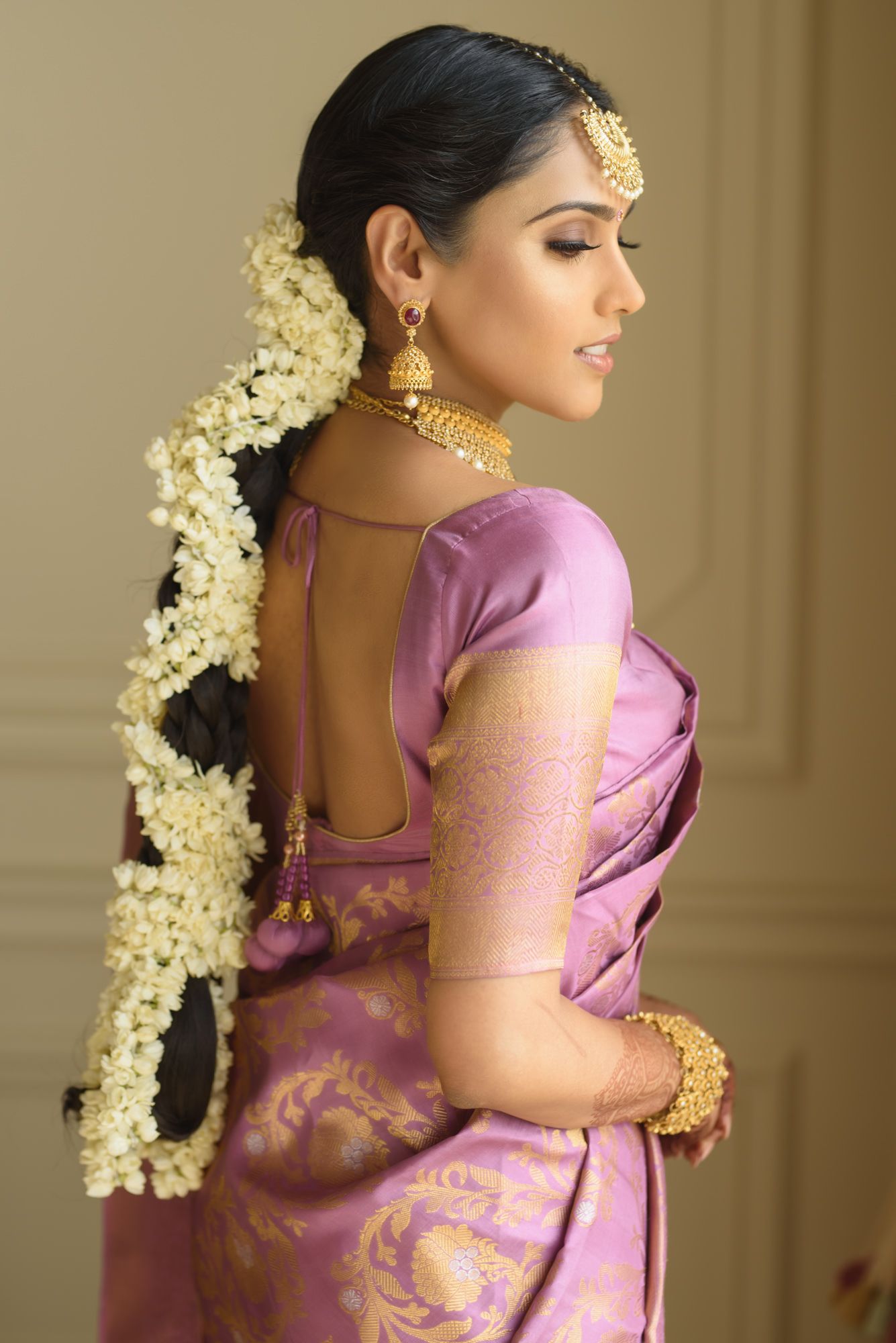 South Indian bride in purple silk saree with jasmine flower braid and gold jewelry back view.