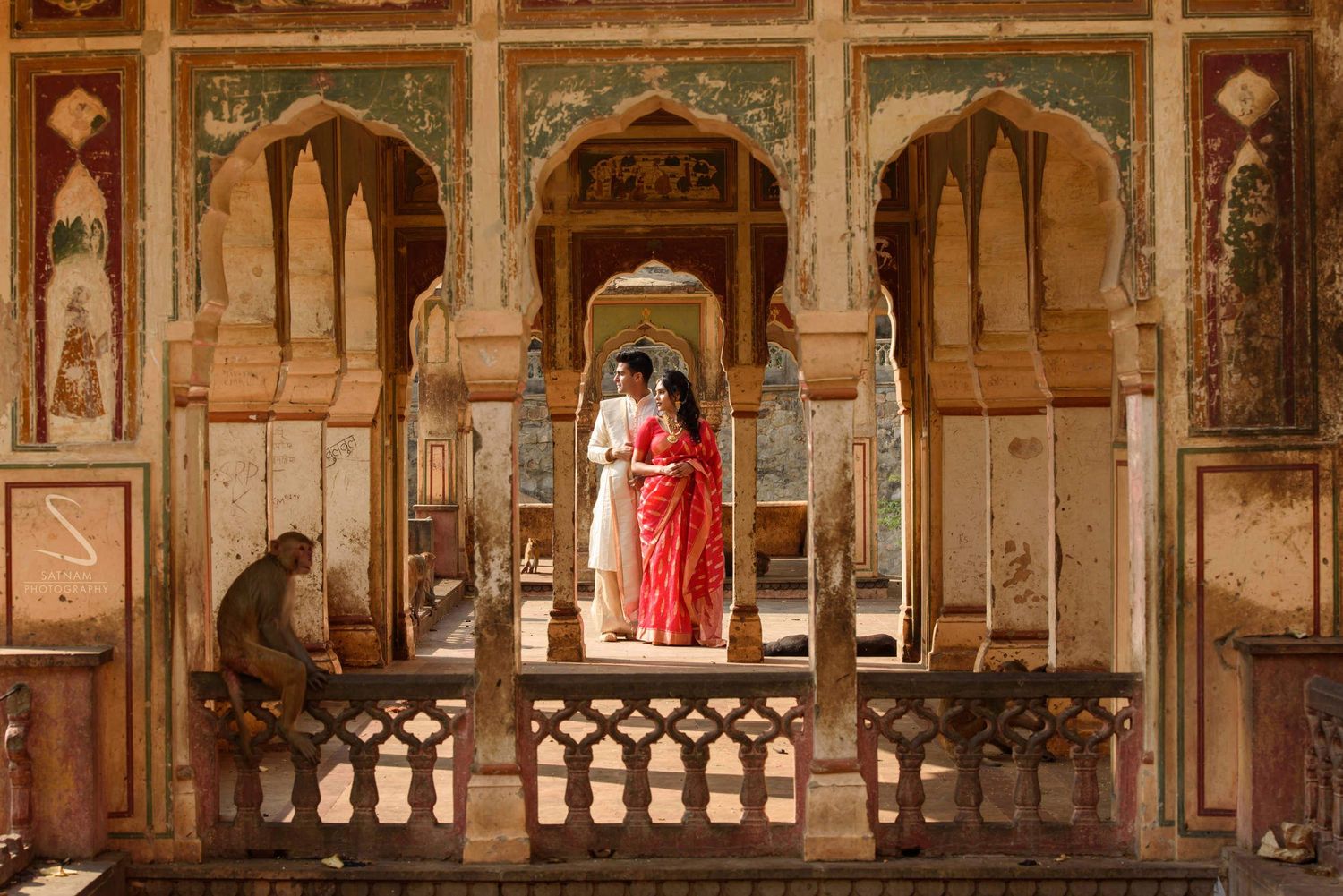 Couple in traditional Indian attire standing in ornate arched corridors of a historic Rajasthani palace.