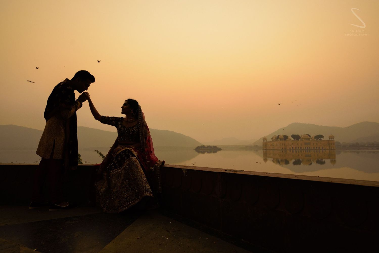 Romantic couple silhouetted at sunset by Jal Mahal lake in Jaipur, India.