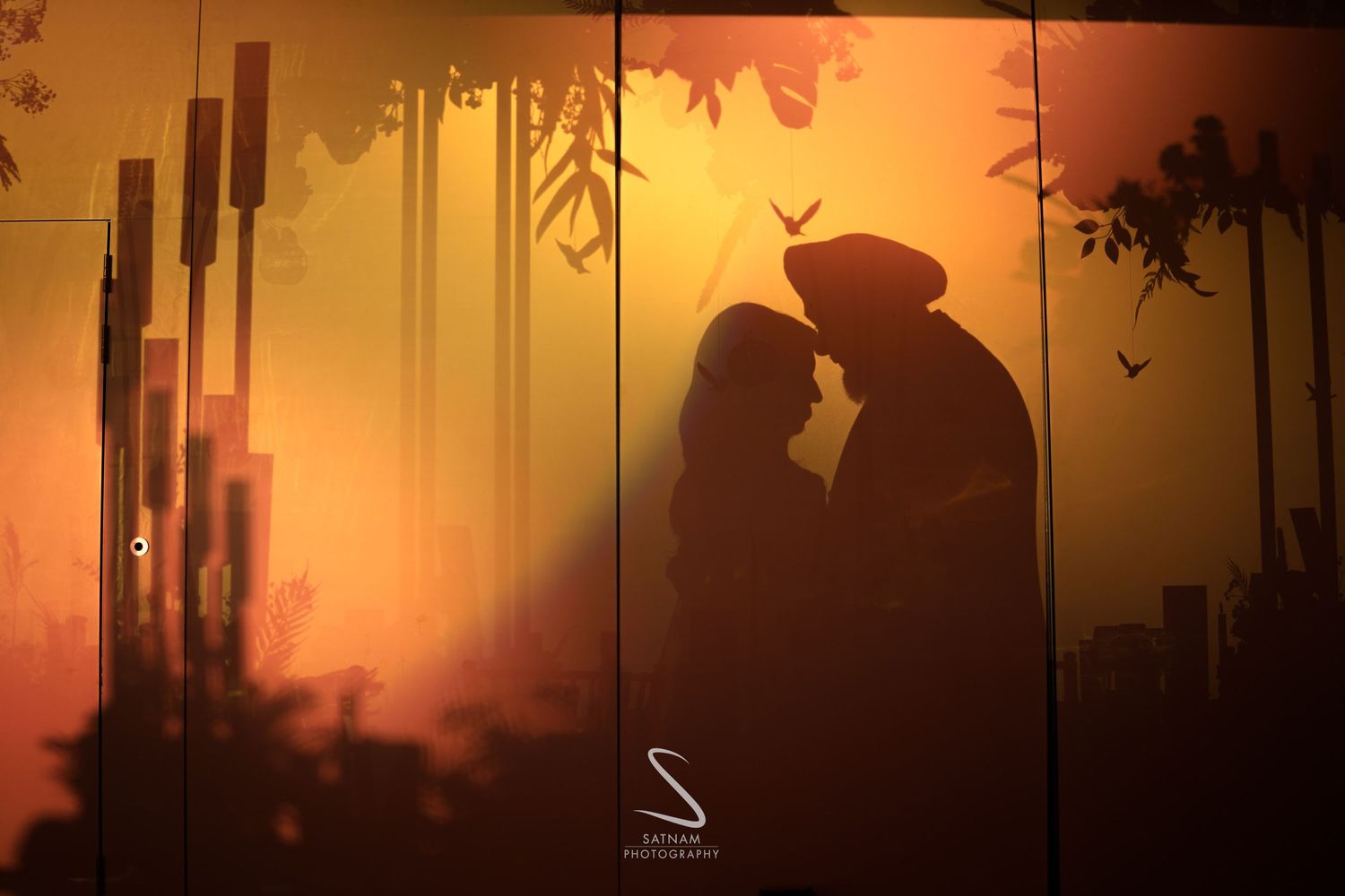Romantic silhouette of couple facing each other against warm orange sunset backdrop mural.
