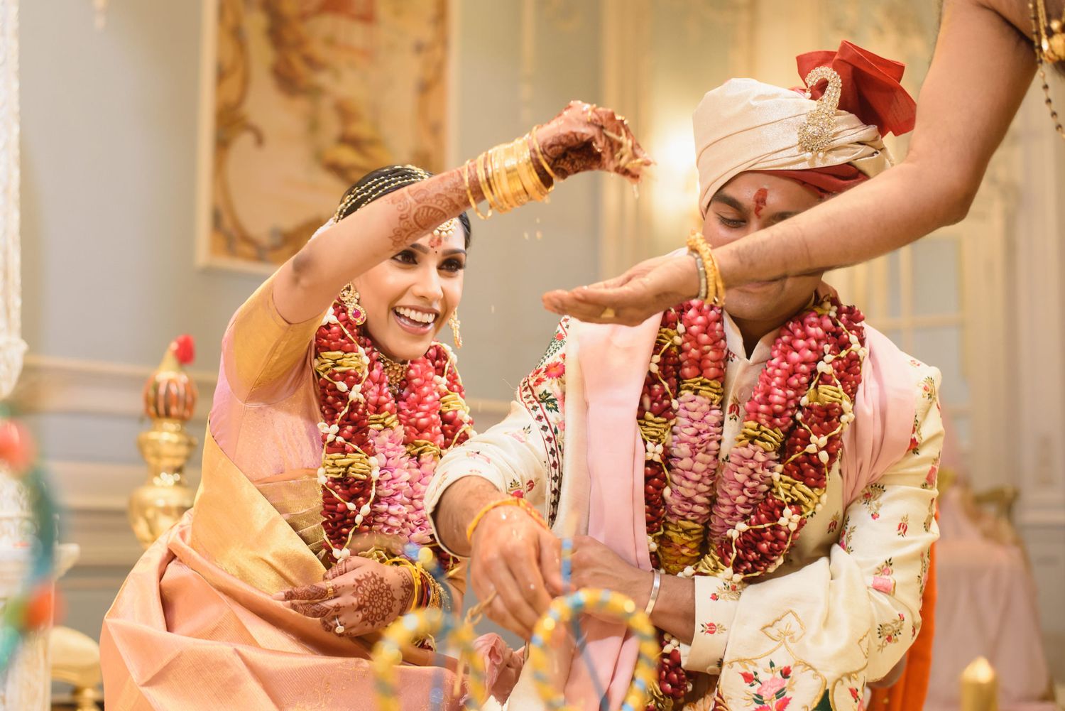 Bride laughs joyfully during traditional Hindu wedding ritual with flower garlands.