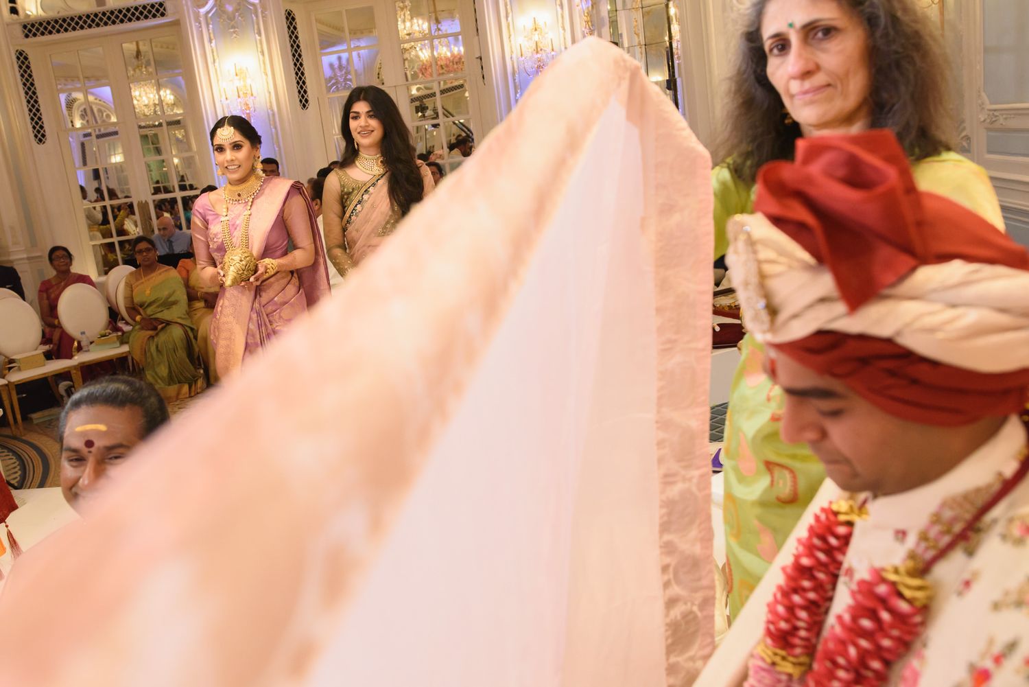 Indian wedding scene with bride in pink saree and groom in red turban during traditional ceremony.