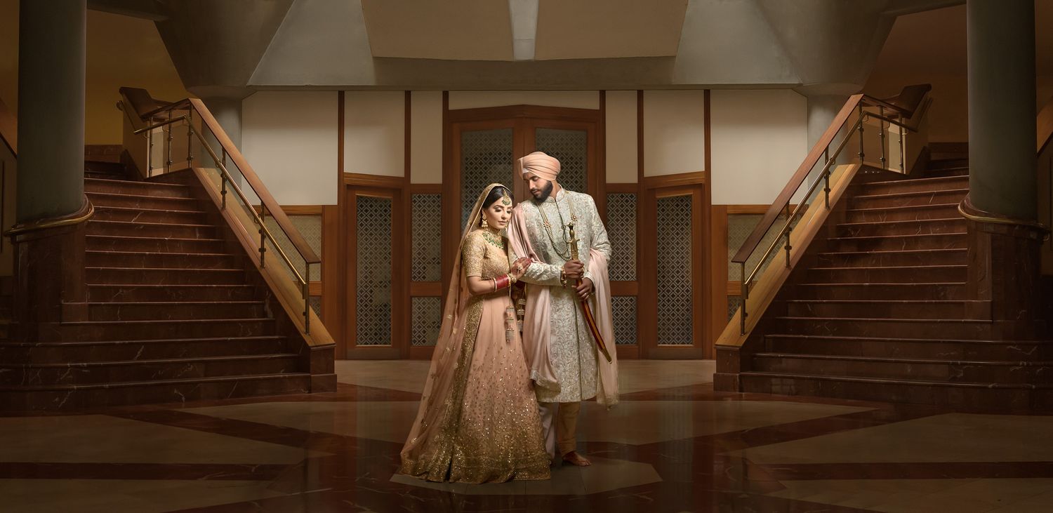Indian bride and groom in traditional wedding attire standing together on elegant staircase backdrop.