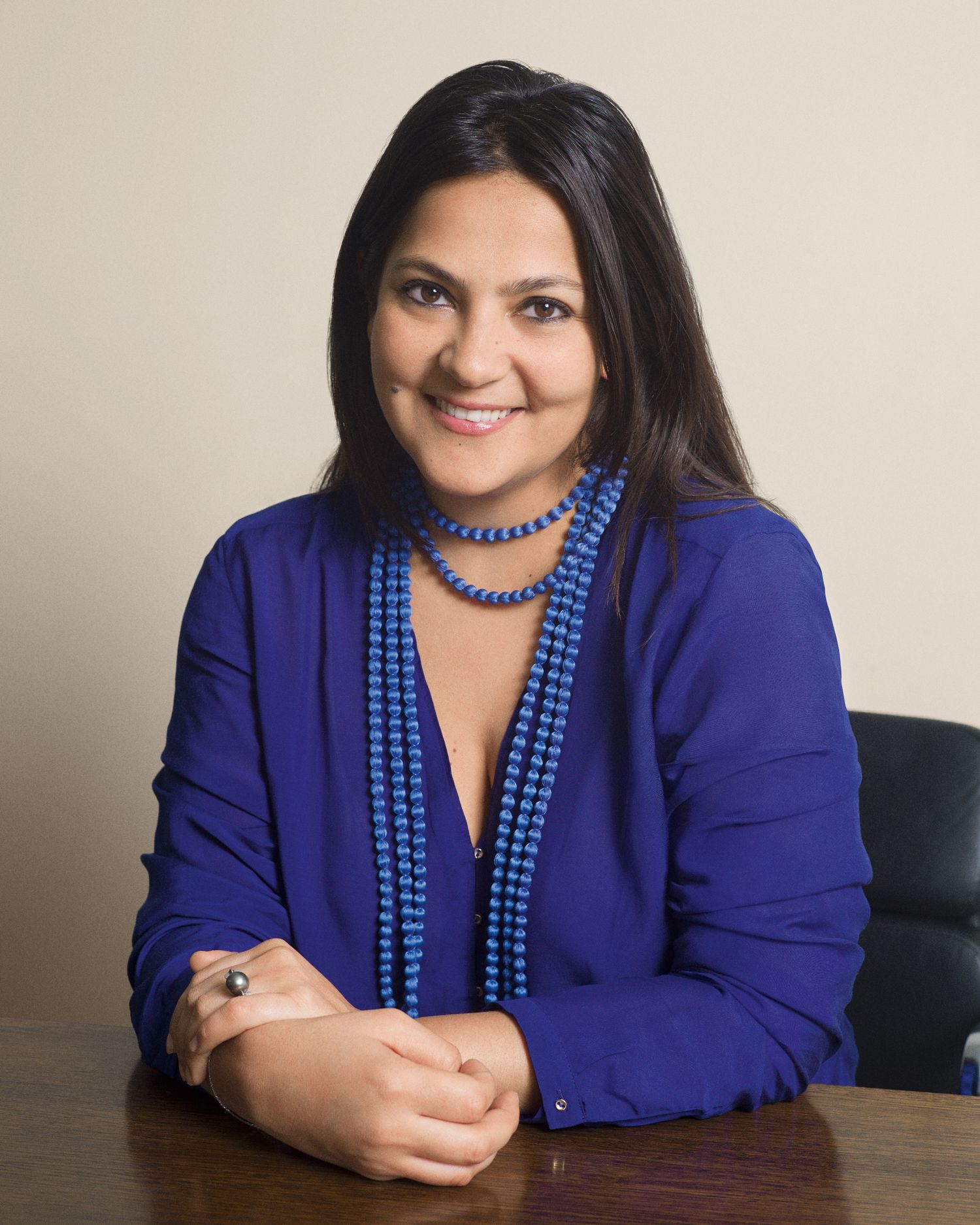 Business Portrait series of someone in royal blue blazer with matching beaded necklace at desk.