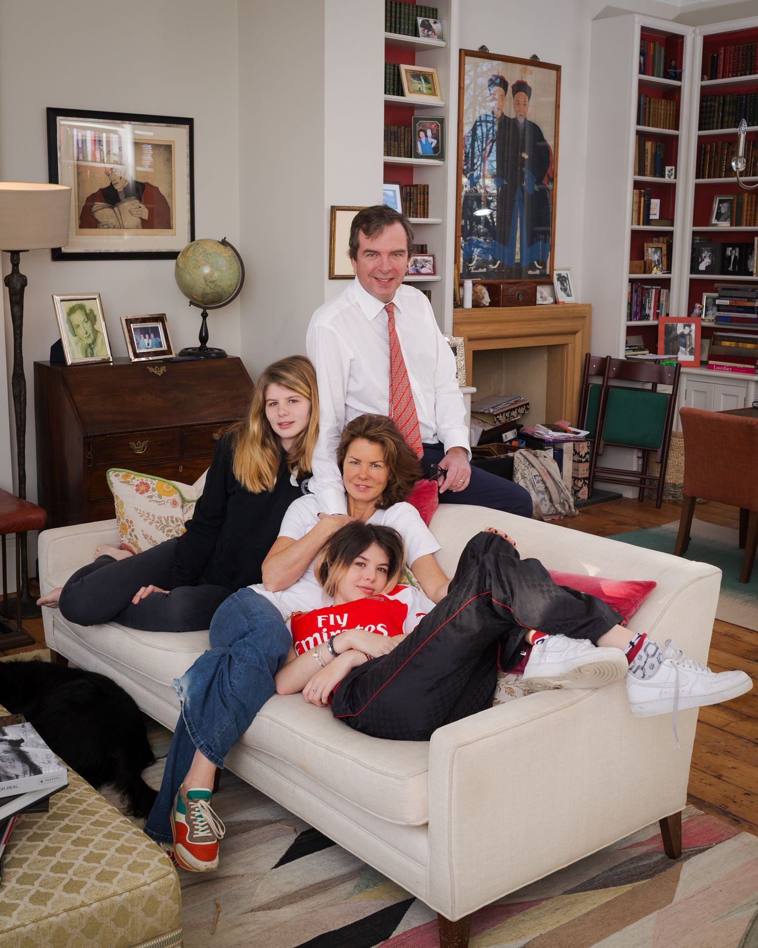 Family lounging on a white sofa in a cozy living room with bookshelves and decorative globe Nottinghill, London..