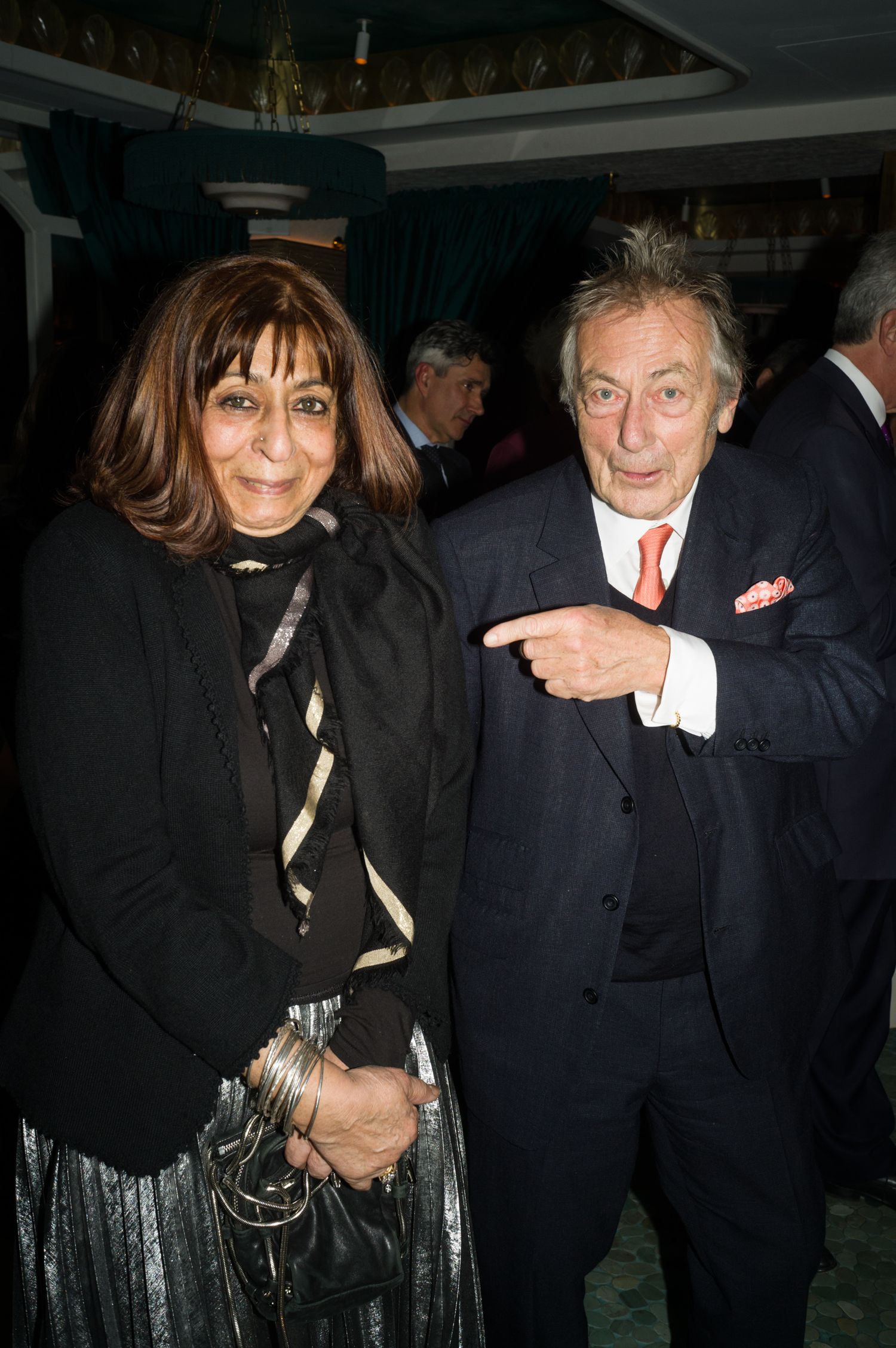 Two people at a formal event, one pointing while wearing a navy suit.
