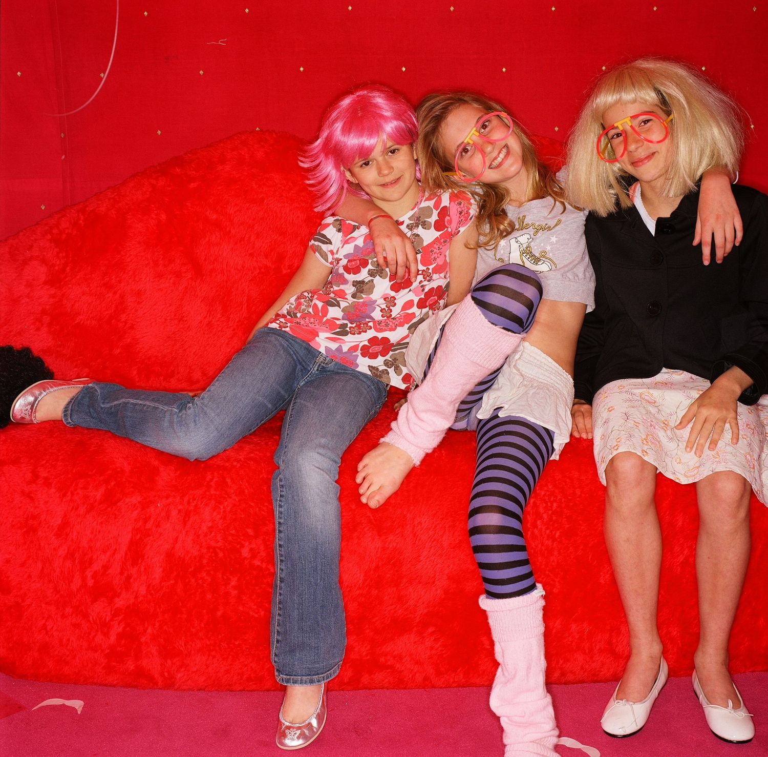 Friends lounging on red couch at casual party gathering.