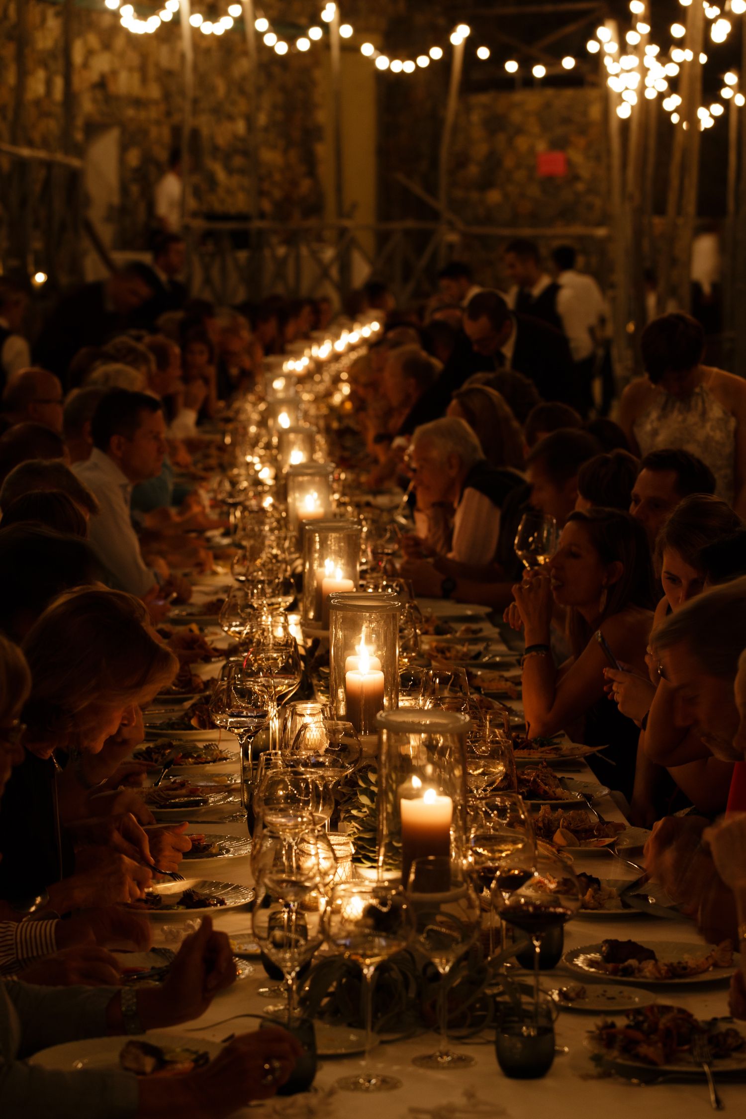 Candlelit wedding reception tables create an intimate ambiance with glowing centerpieces and string lights overhead.