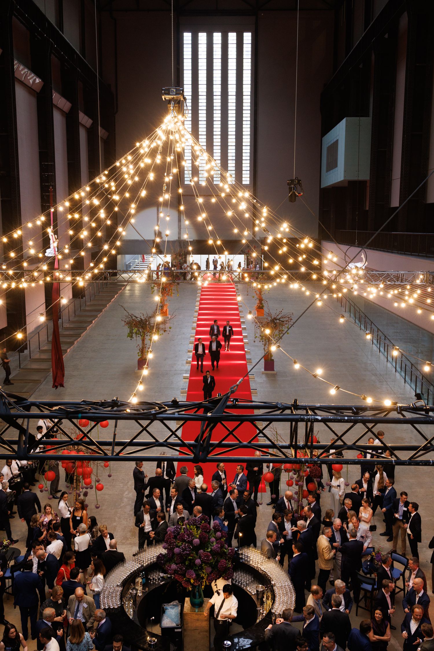 Wedding reception venue decorated with string lights and a red carpet runway under high industrial ceilings.