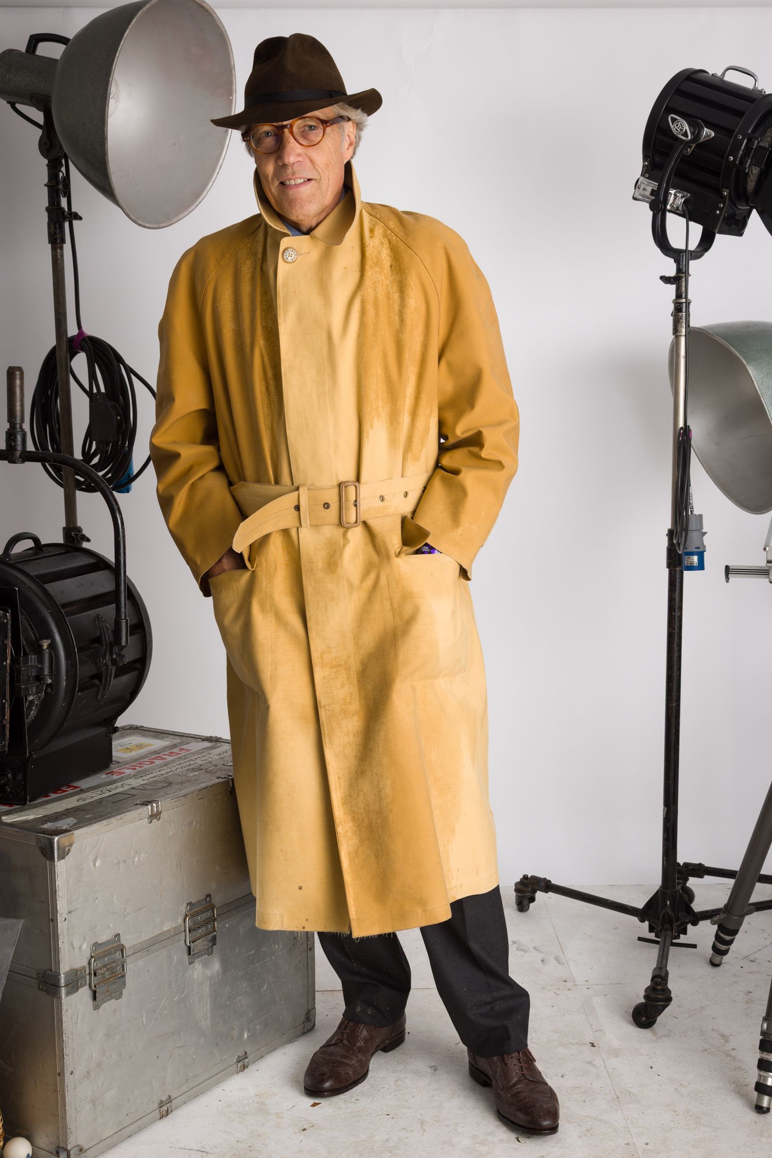 Studio portrait of Duke of Richmond in tan trench coat and brown fedora posing with photography equipment. Goodwood Revival 2024