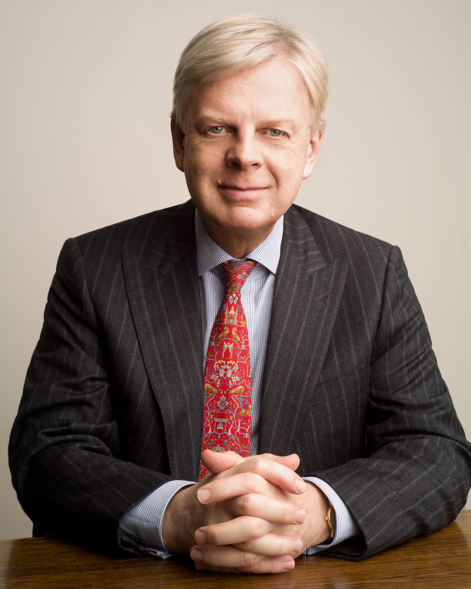 Professional headshots of someone in pinstripe suit with red tie at desk.