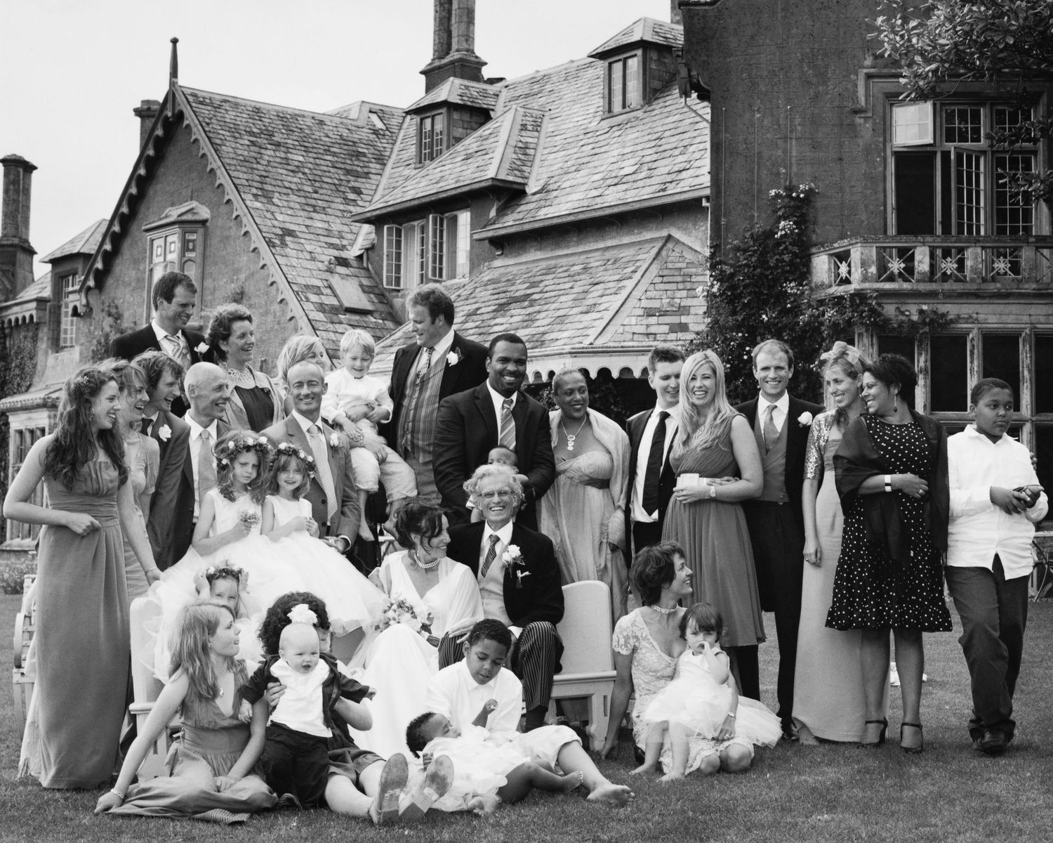 Large vintage wedding party gathered outside historic building for group photo.