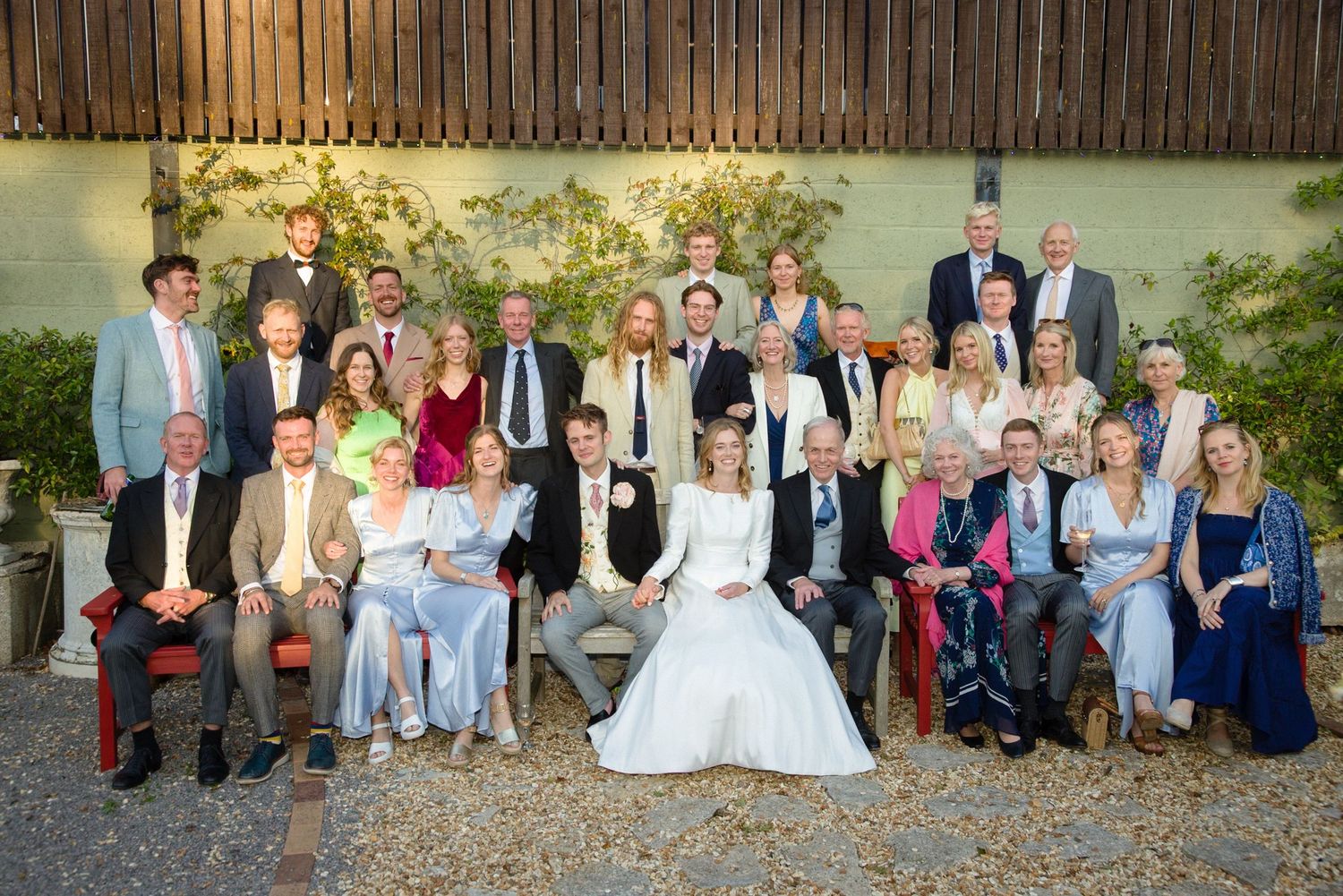 A large wedding party poses for a formal group photo outdoors.