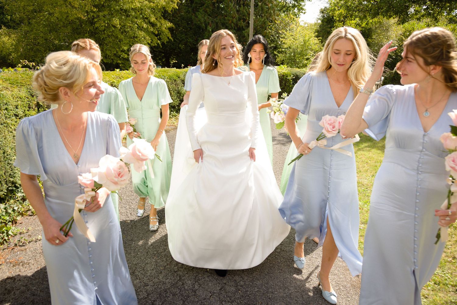 A bride and bridesmaids in pastel blue dresses walking together outdoors on an English summer sunny day.