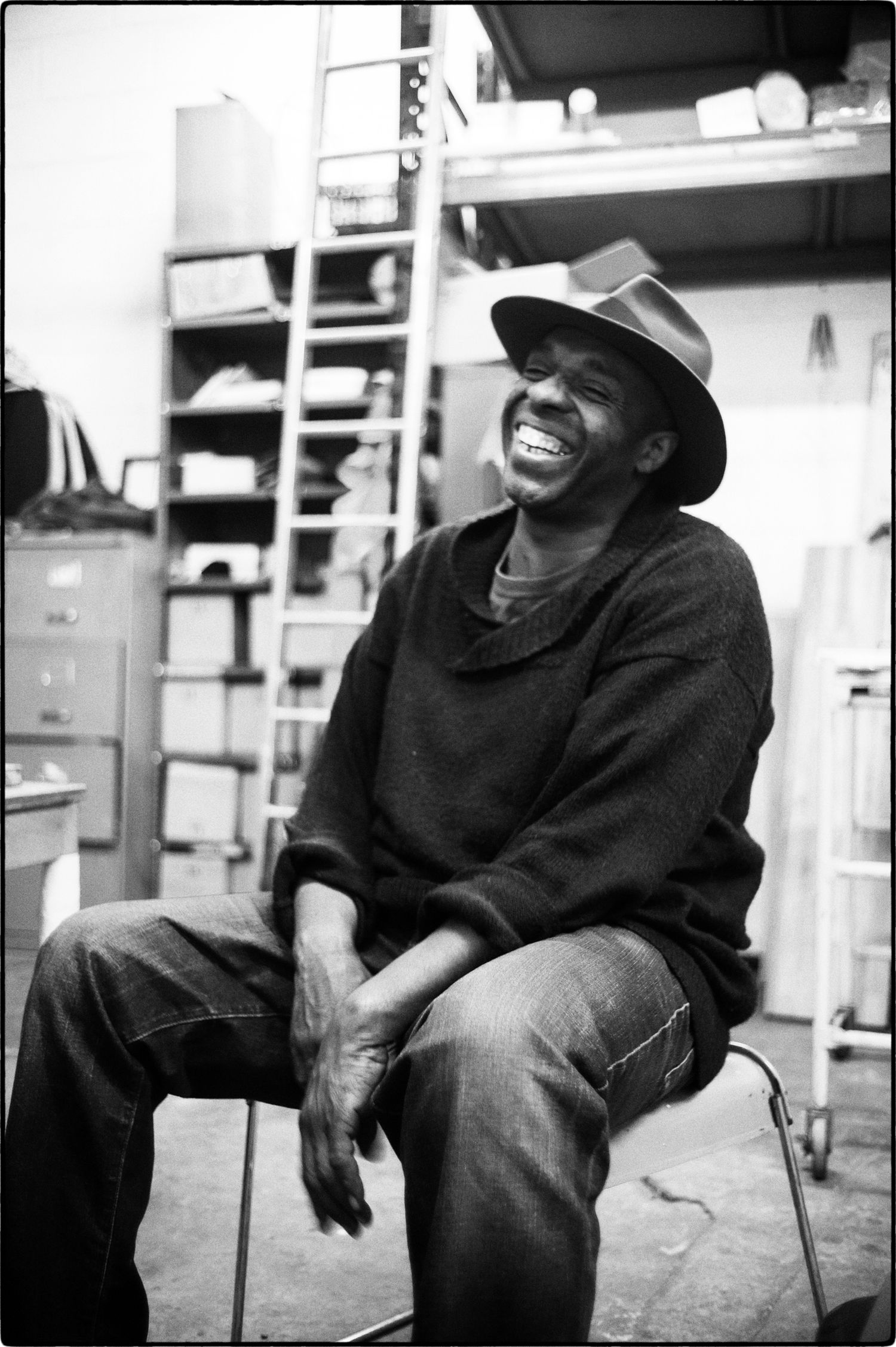 Black and white candid photos of artist Cedric Christie laughing while seated in casual clothing.