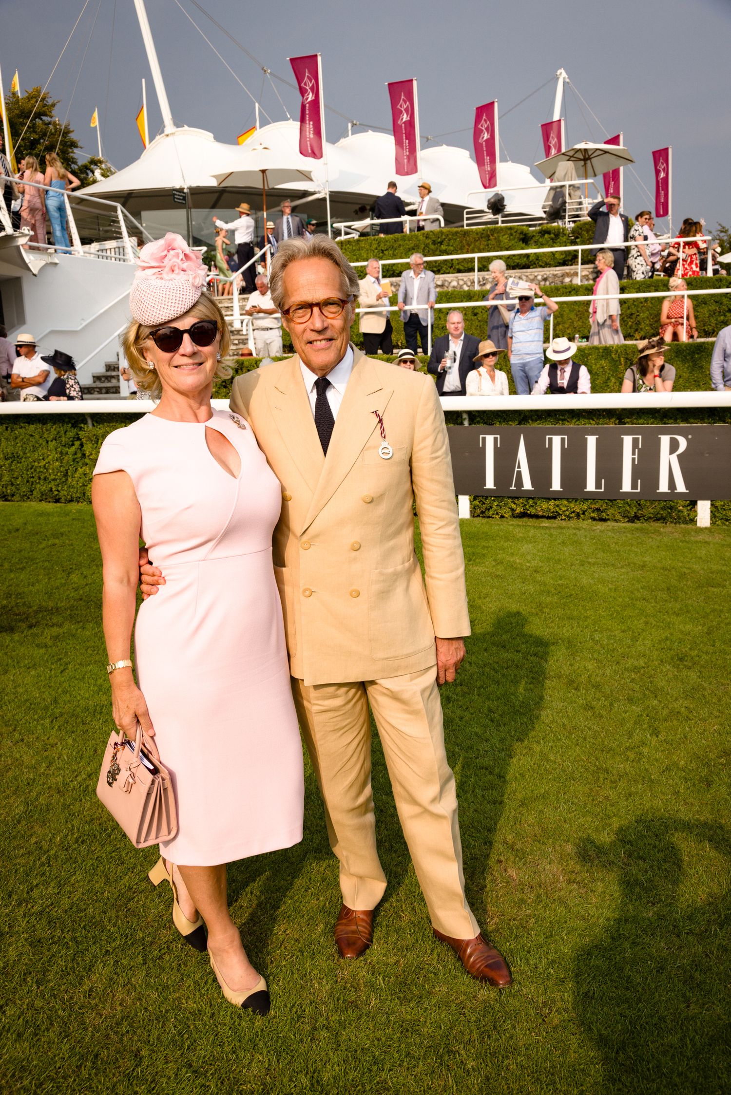 Couple in coordinated pink and tan outfits pose on grass at an outdoor summer event.