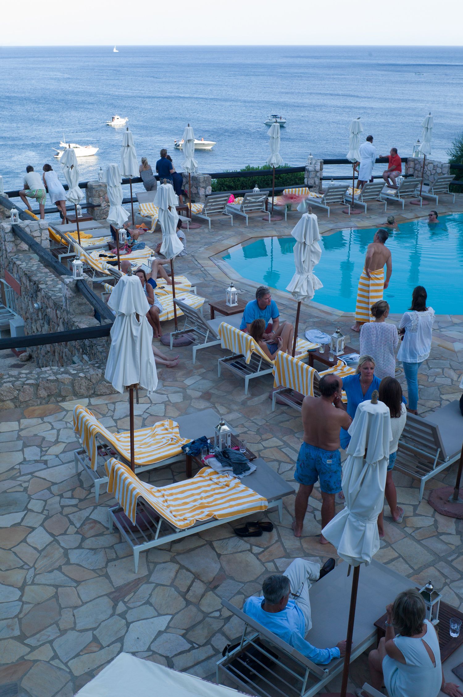 Resort pool deck overlooking the ocean with lounge chairs and umbrellas at sunset.