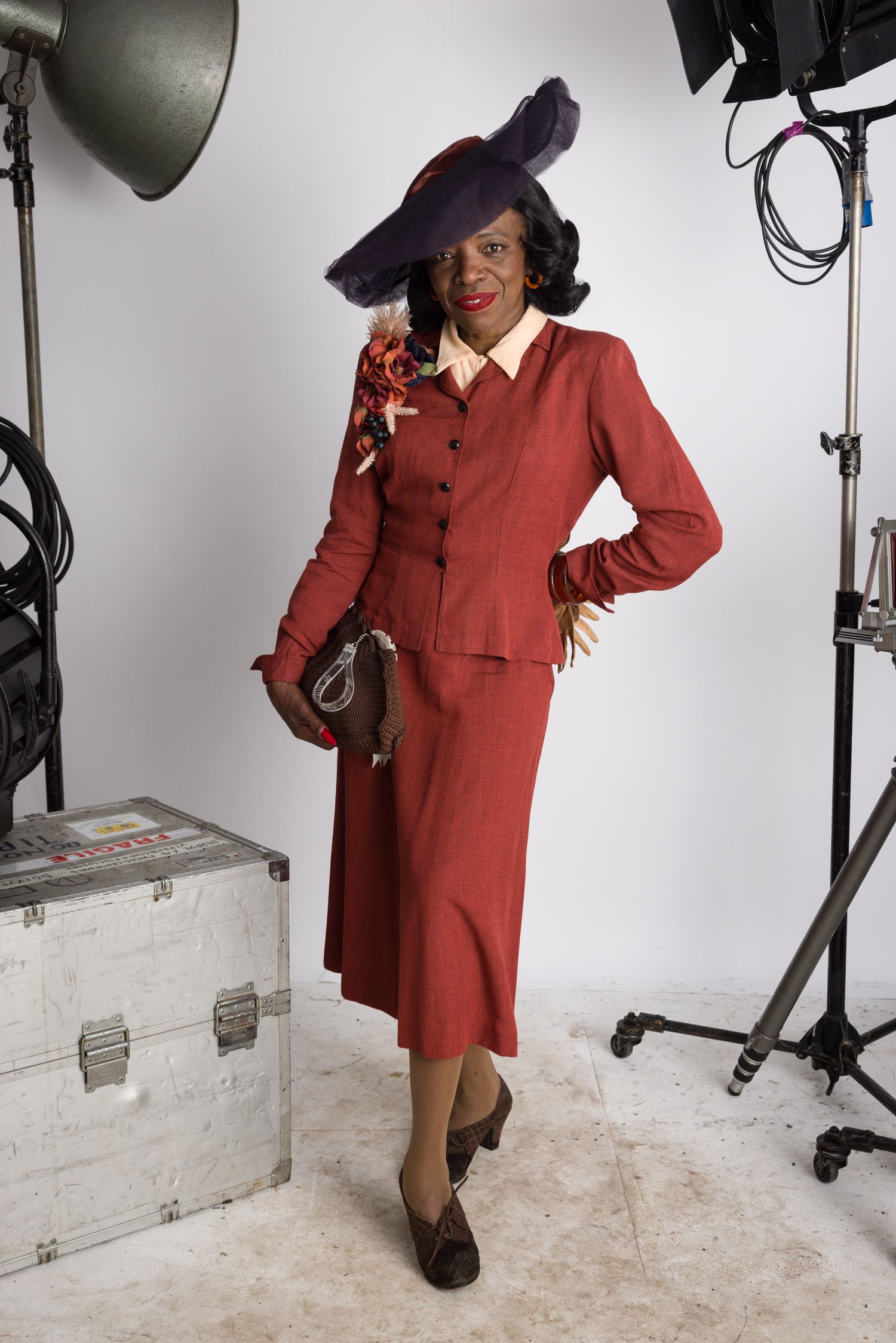 Vintage 1940s style fashion photo featuring burgundy suit and purple feathered hat at Goodwood Revival 2024.