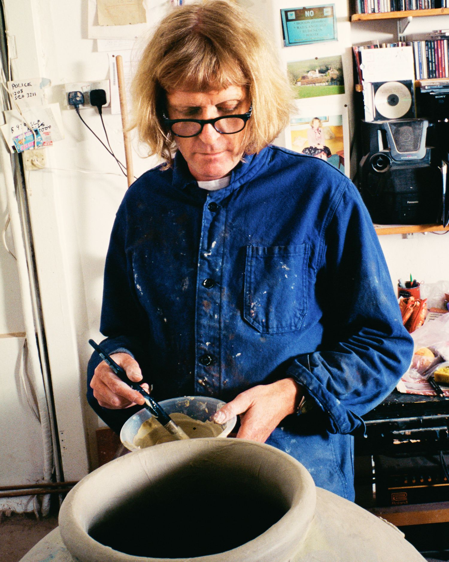 Series showing artist Grayson Perry working with clay on pottery wheel wearing denim overall.