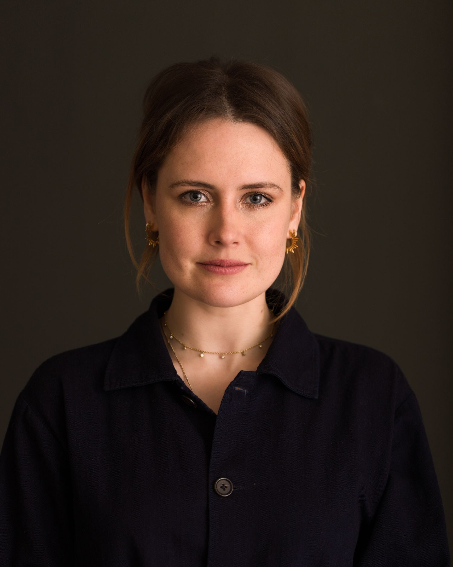 Dramatic portrait series Honor Palmer-Tompkinson against dark background in black clothing.