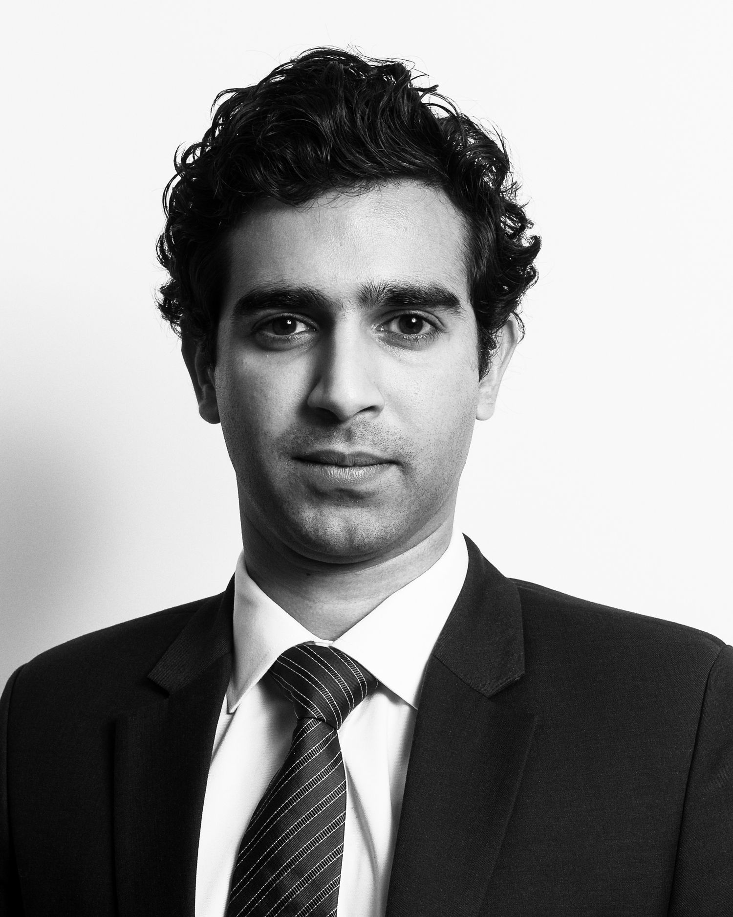 Business headshot Black and white portrait series of young man in suit and tie with dark curly hair.