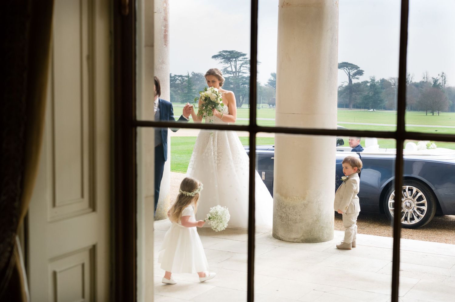 Wedding venue entrance with white columns and glass doors captured through window frame.