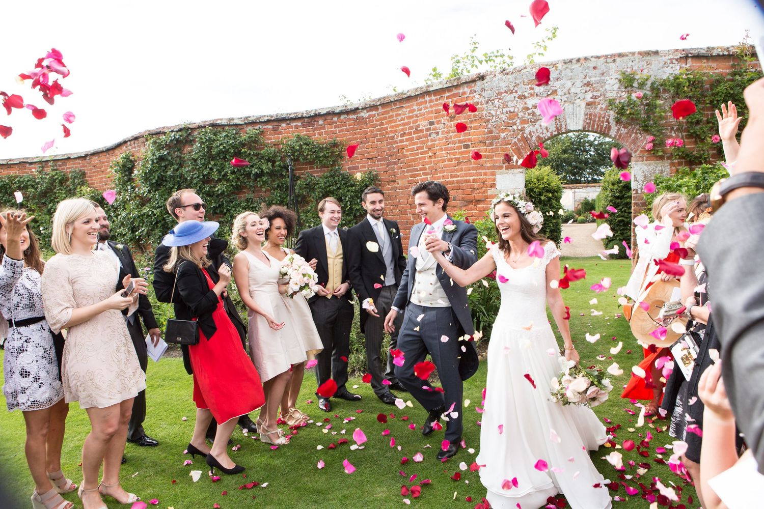 Wedding guests shower newlyweds with pink rose petals in an outdoor celebration.