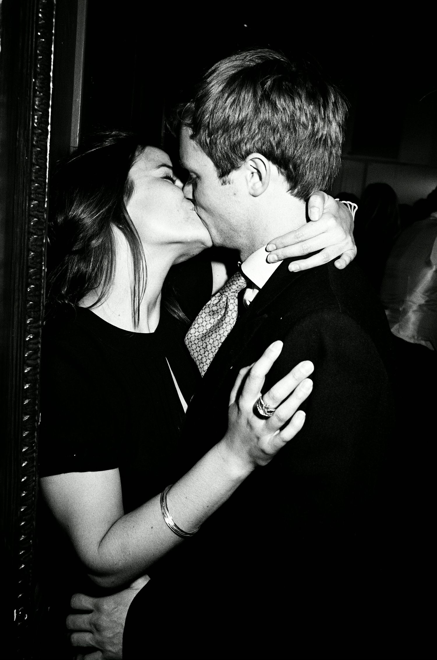 A romantic black and white photo of a couple sharing an intimate kiss at event lit with on camera flash .
