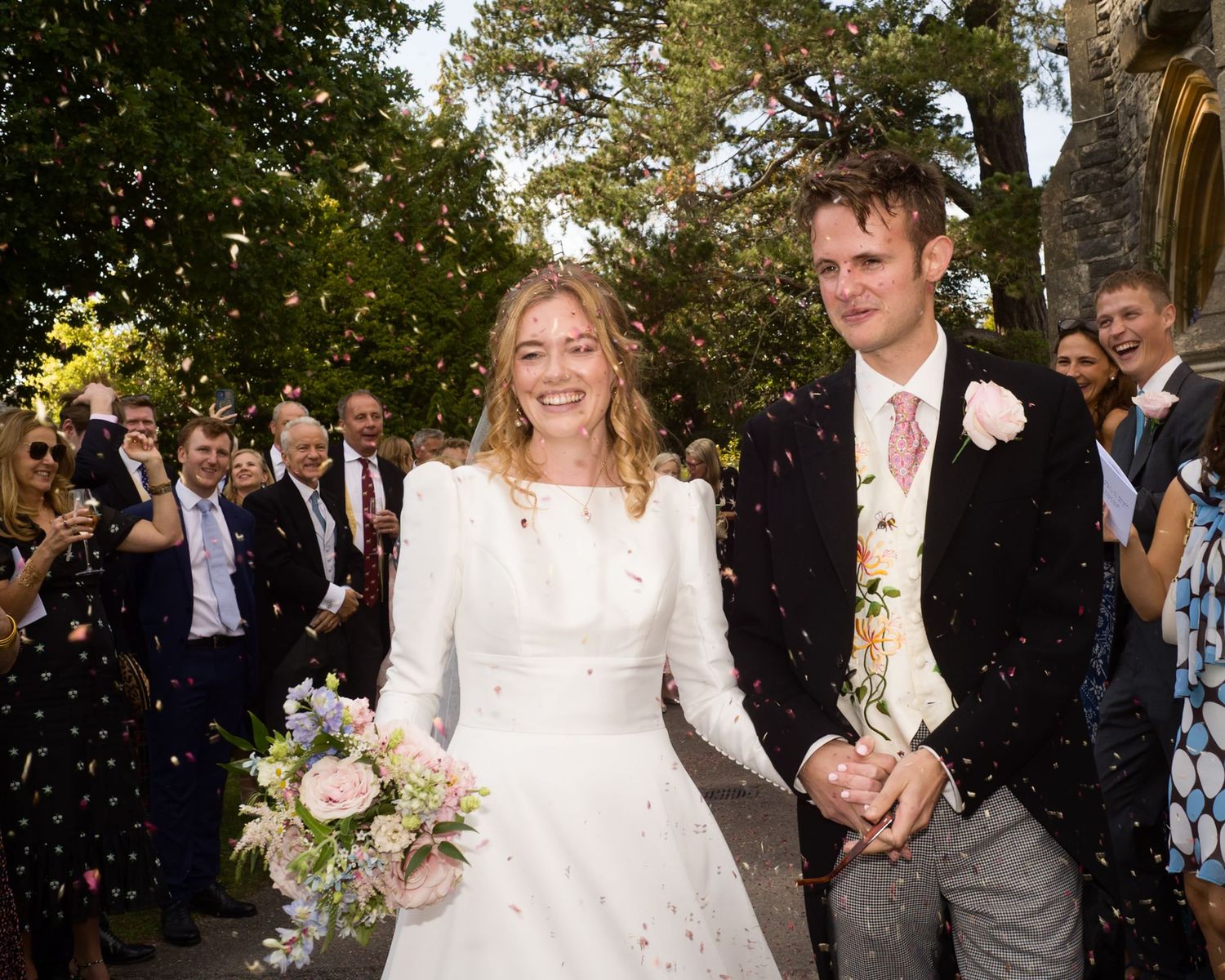 A newlywed couple exits their wedding ceremony as guests throw confetti in celebration.