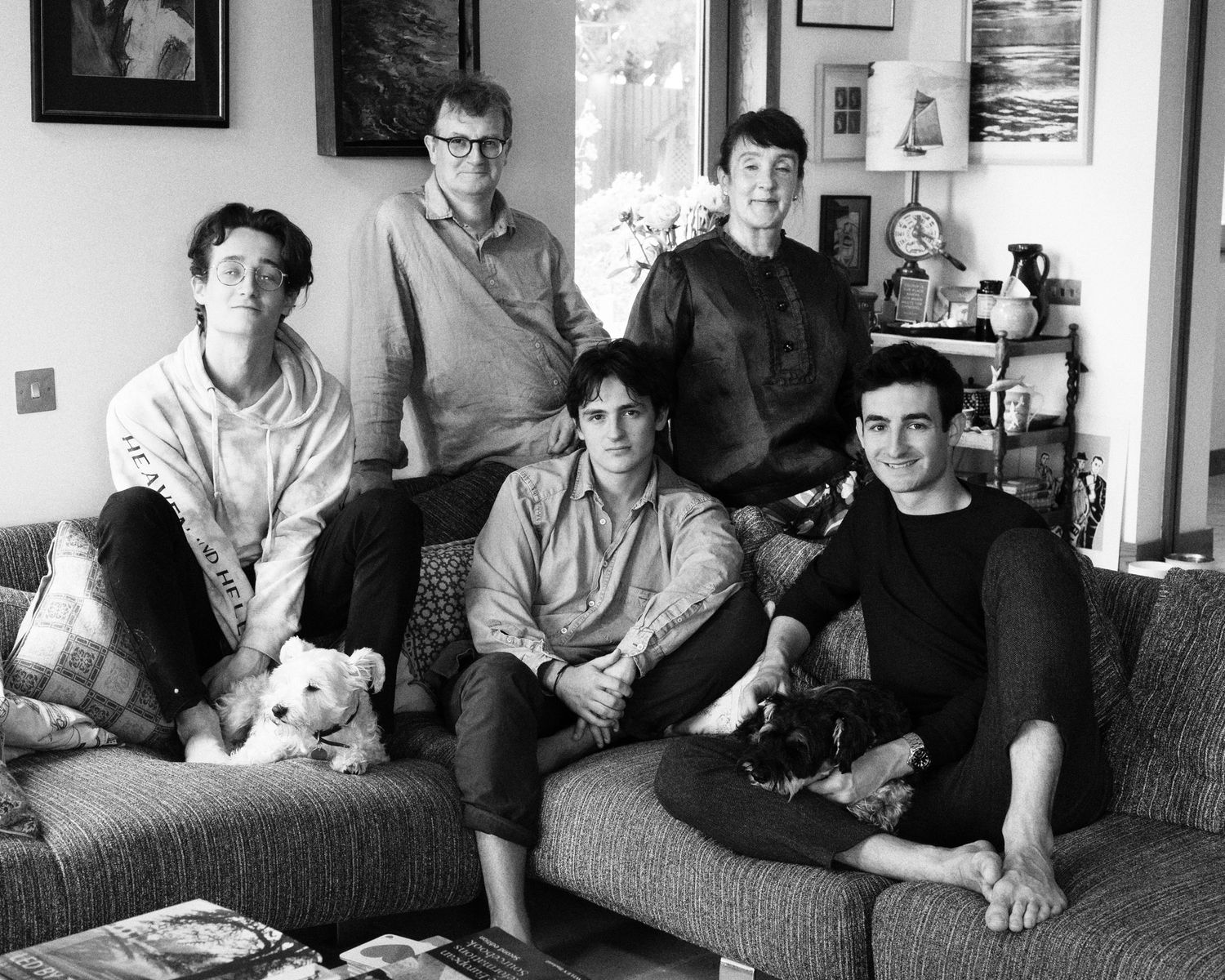 Family group relaxing together on a couch with a small white dog in a casual home setting.