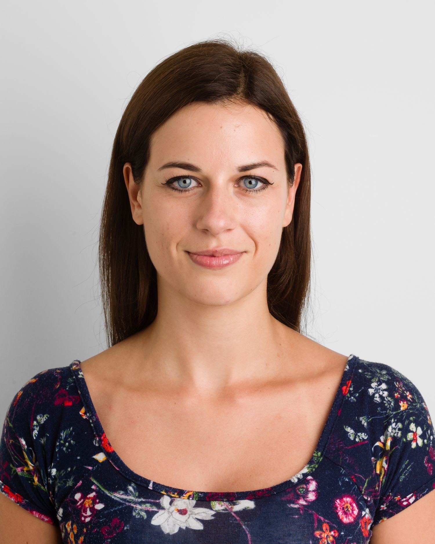 Business headshot Portrait of a person in navy floral print top with long brown hair against neutral background.