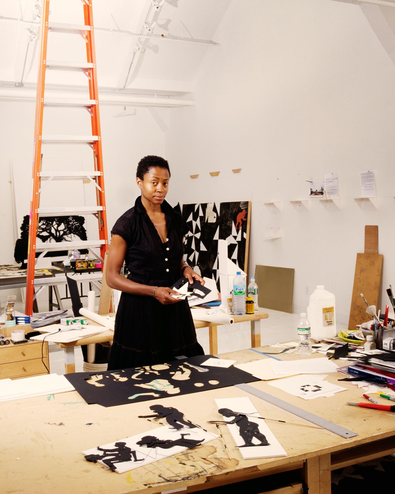 Artist Cara Walker working in her New York studio with orange ladder and artwork displayed on walls and tables.