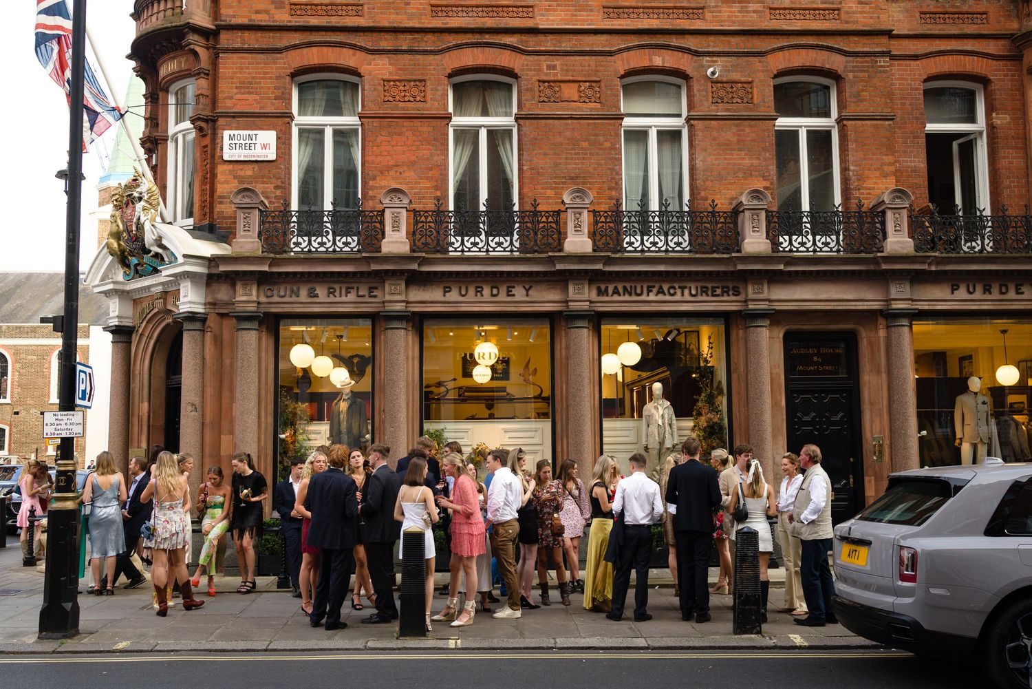 Street view of a classic red brick building Mayfair, London with people gathered outside storefronts.