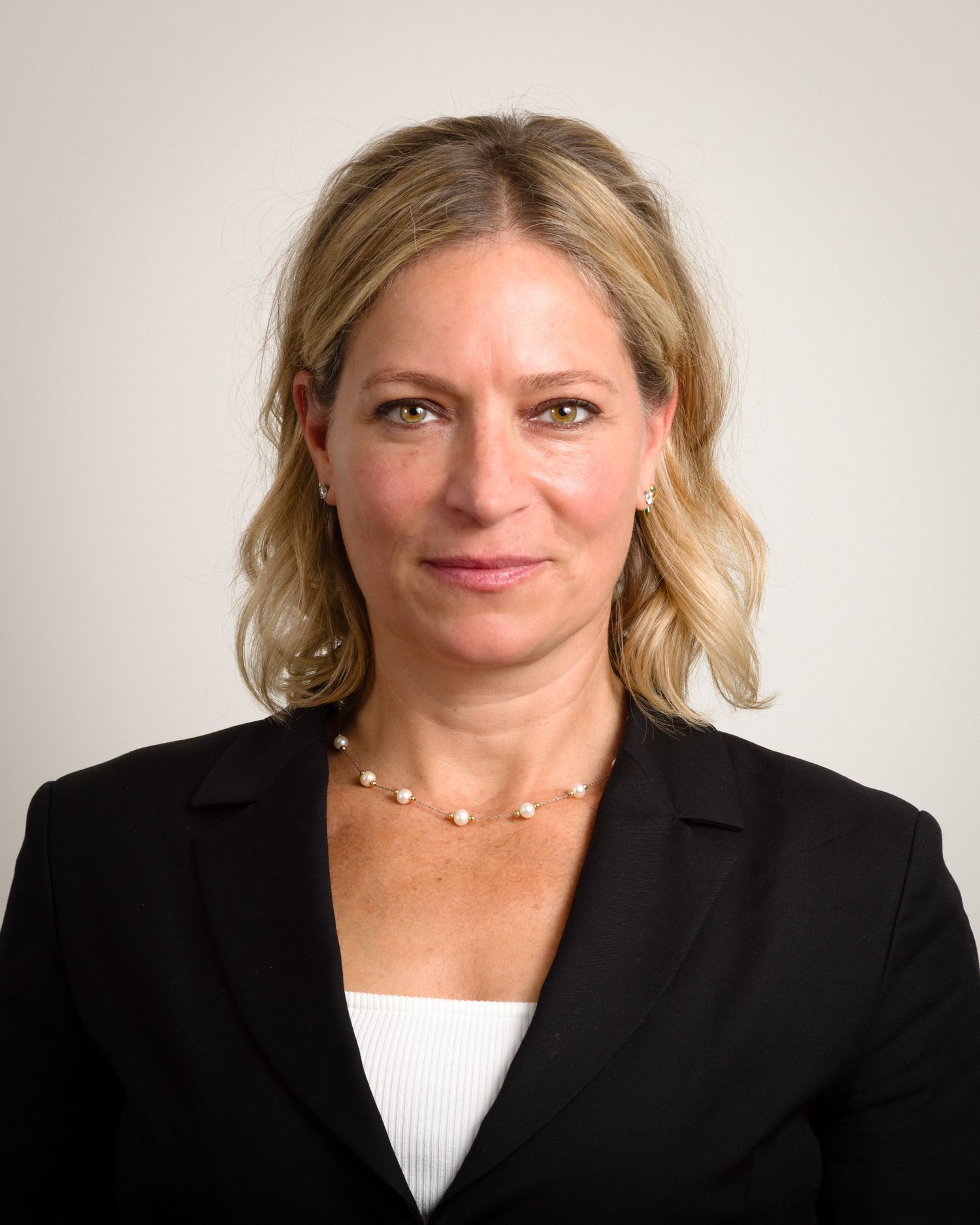 Business portrait series of woman in black blazer with blonde hair against neutral backdrop.