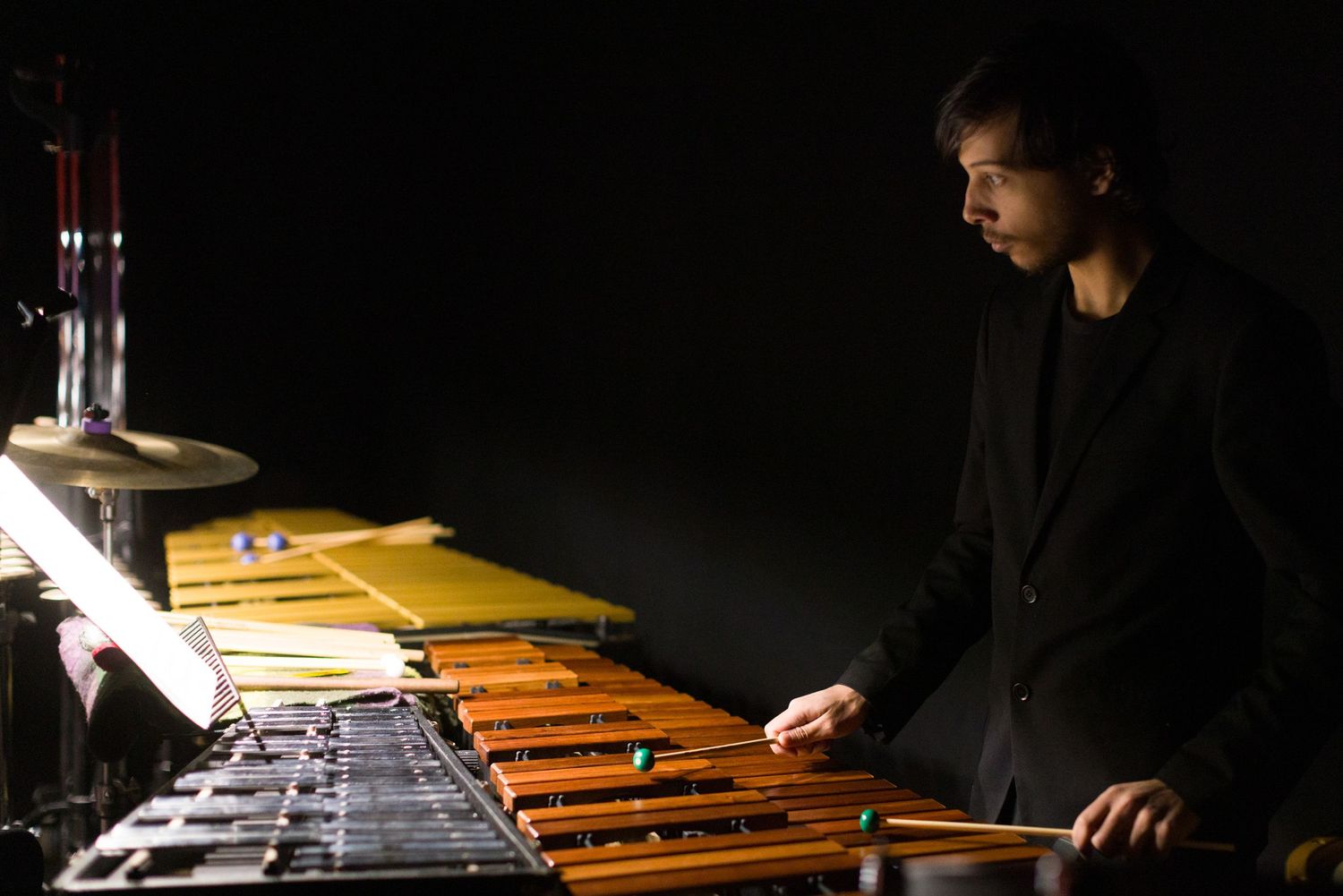 Musician playing xylophone in dramatic lighting against black background.