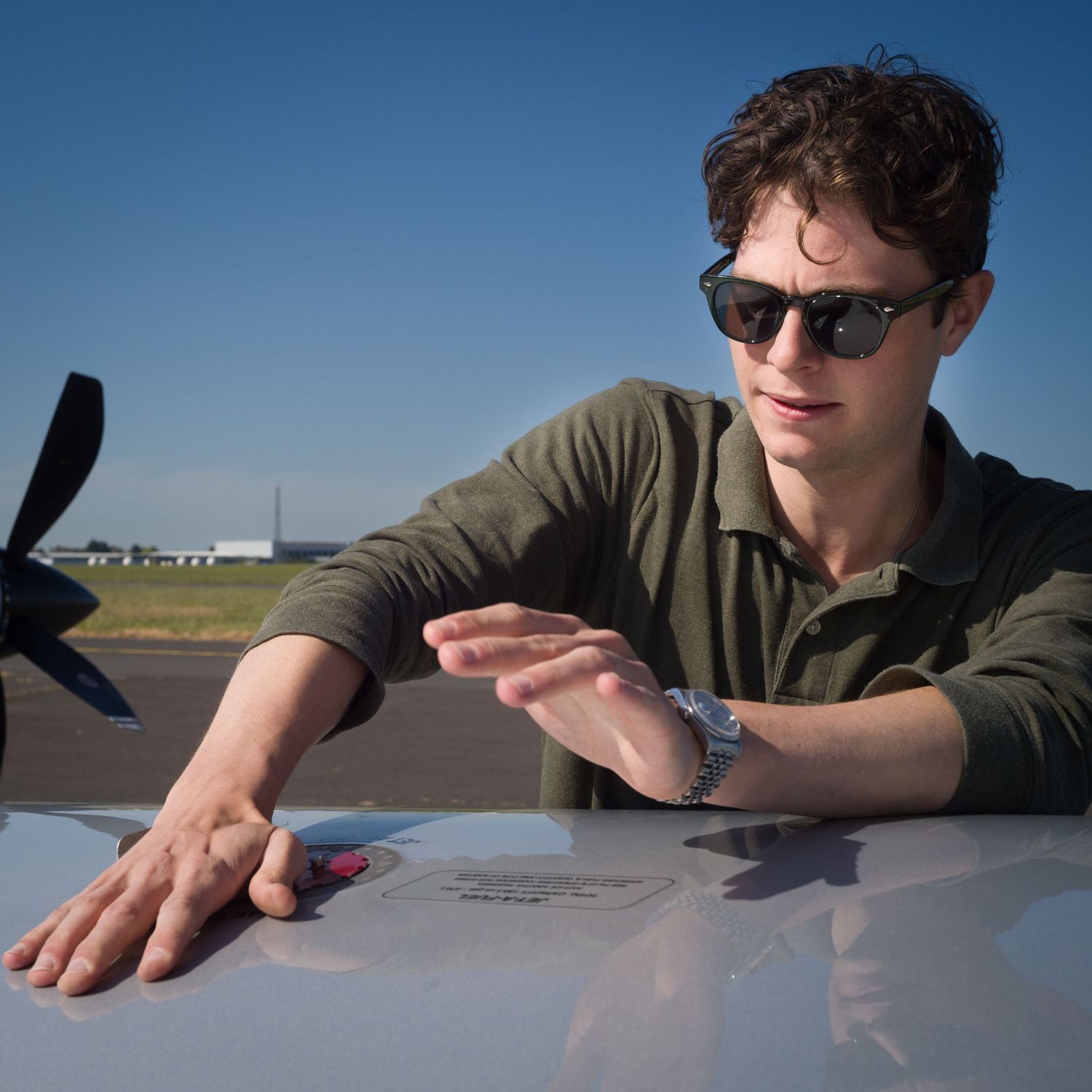 Person in sunglasses leaning over TBM wing in multiple action shots against blue sky.