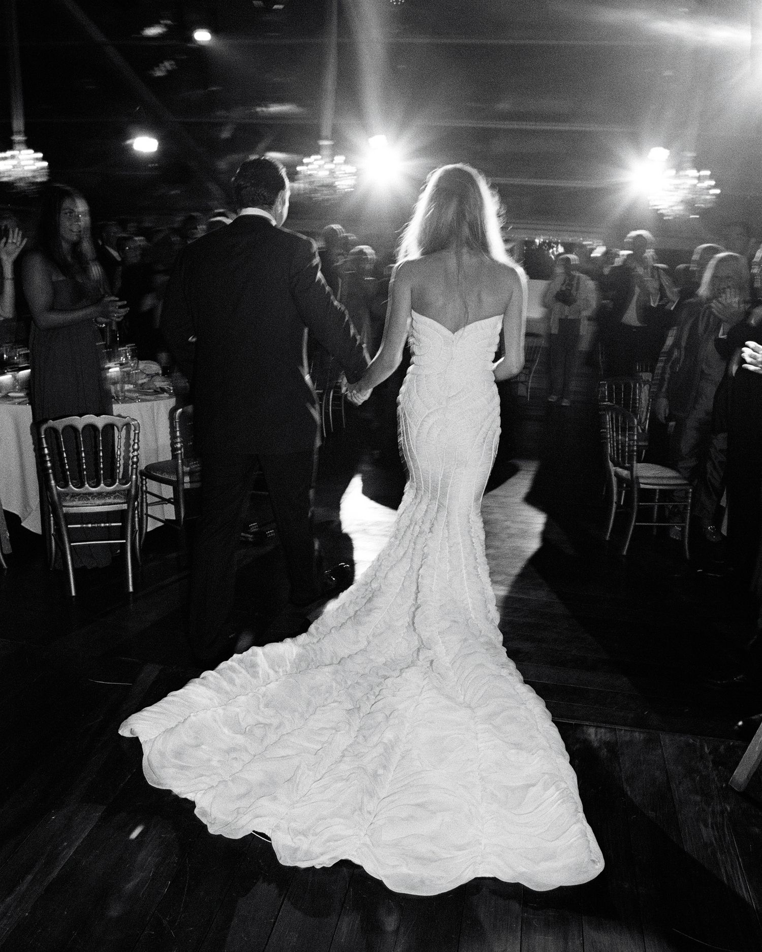 Bride dancing in a flowing white wedding dress on a dark dance floor.