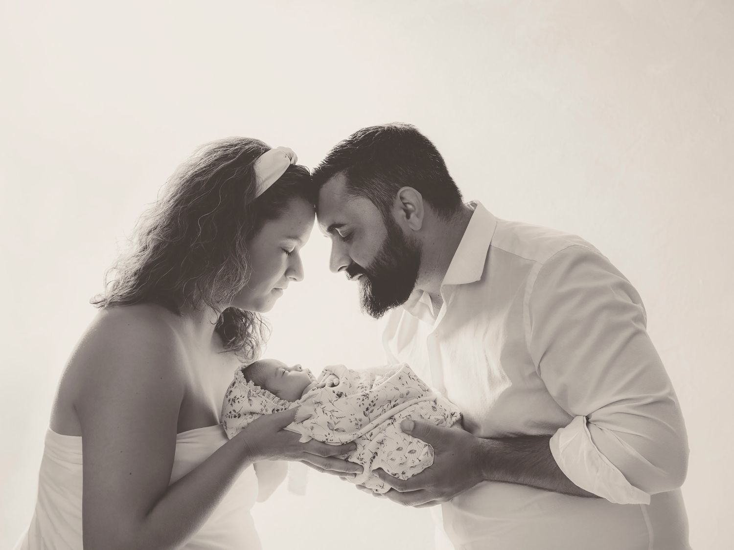 Foto en blanco y negro de papas mirando con ternura a su bebé recién nacido en un retrato de estudio.