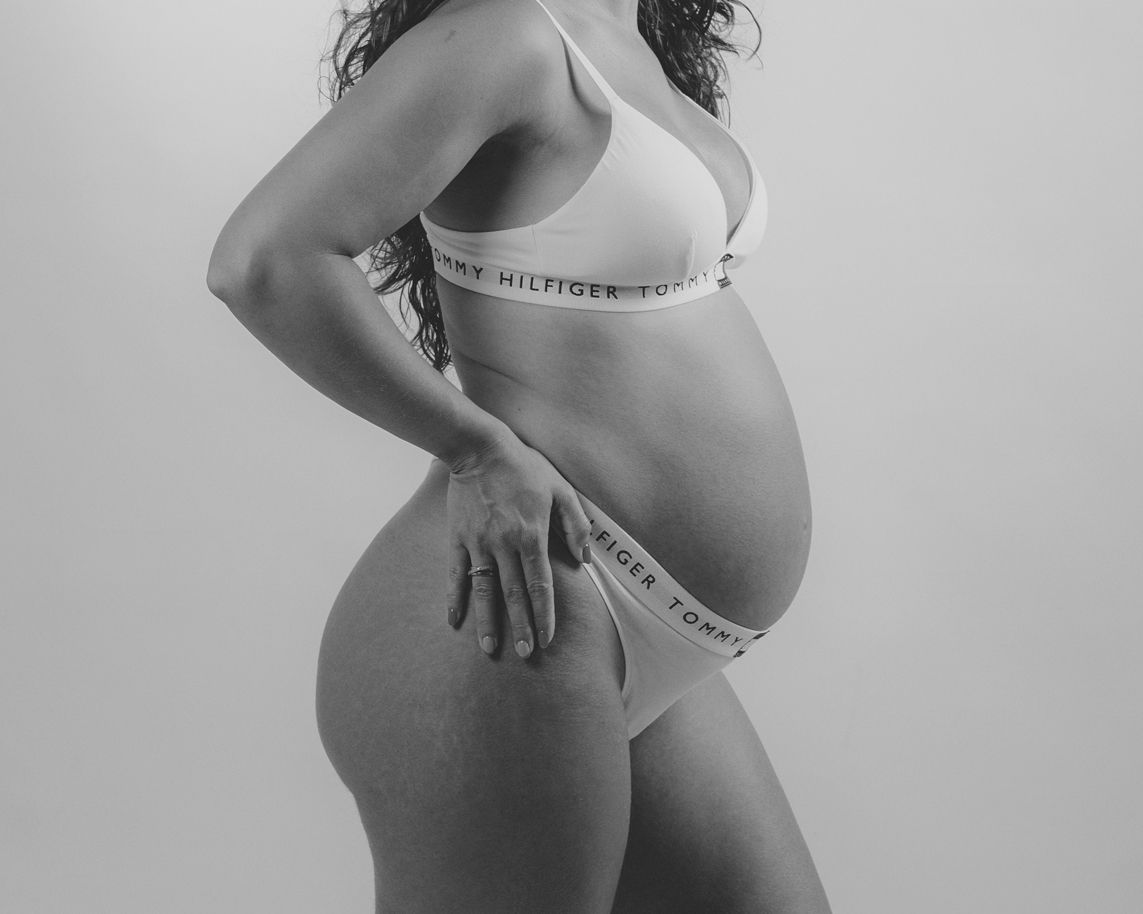 Fotografía de maternidad en blanco y negro de la barriga de una mujer embarazada en ropa interior, posando de lado.