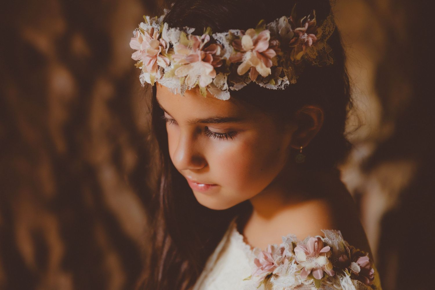 Retrato de comunión de una niña con una delicada corona floral rosa sobre un fondo con efecto bokeh suave.