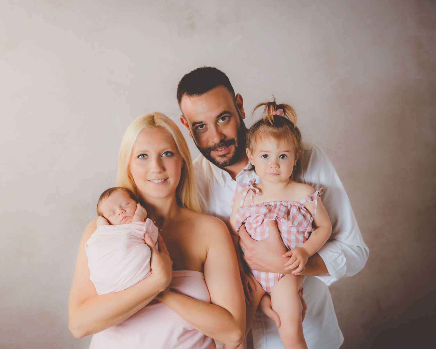 Retrato familiar feliz con los padres sosteniendo a su bebé recién nacida y a su hija pequeña vestida de rosa.