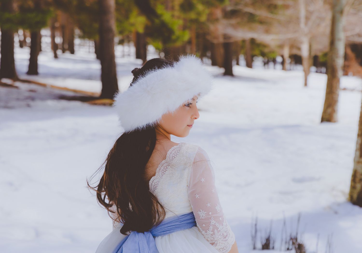 Niña con vestido de comunión y gorro de pelo blanco en un bosque nevado en su sesión de fotografía en el puerto de la Ragua de Almería.