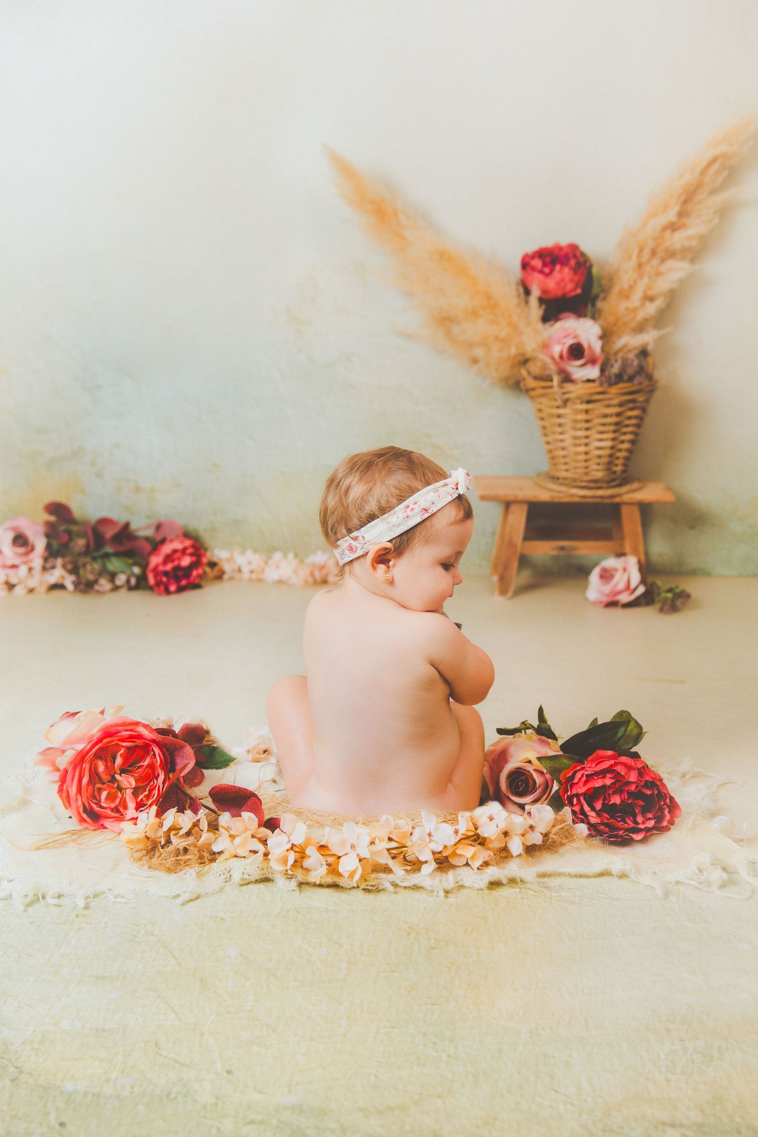 Una bebé con una diadema floral posa entre rosas y peonías en una preciosa sesión de fotos de estilo bohemio.
