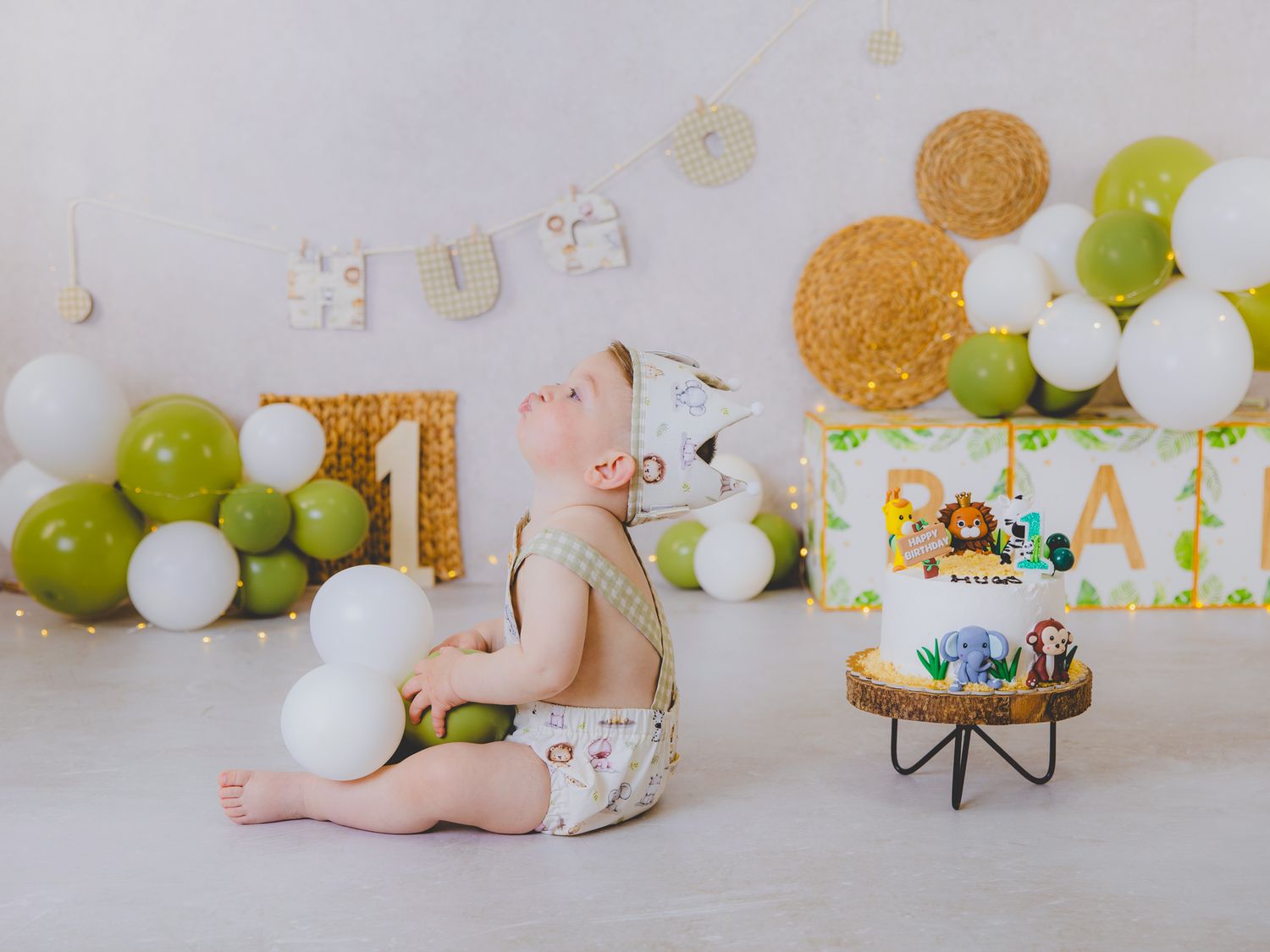 Reportaje fotográfico de un bebé de su primer cumpleaños con temática de la selva, globos verdes y blancos y un pastel decorado.