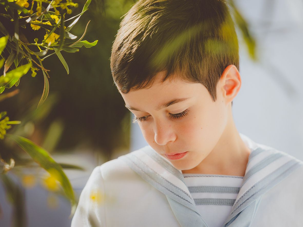 Primer plano de perfil de un niño de comunión con su rostro enmarcado con ramas de un árbol.