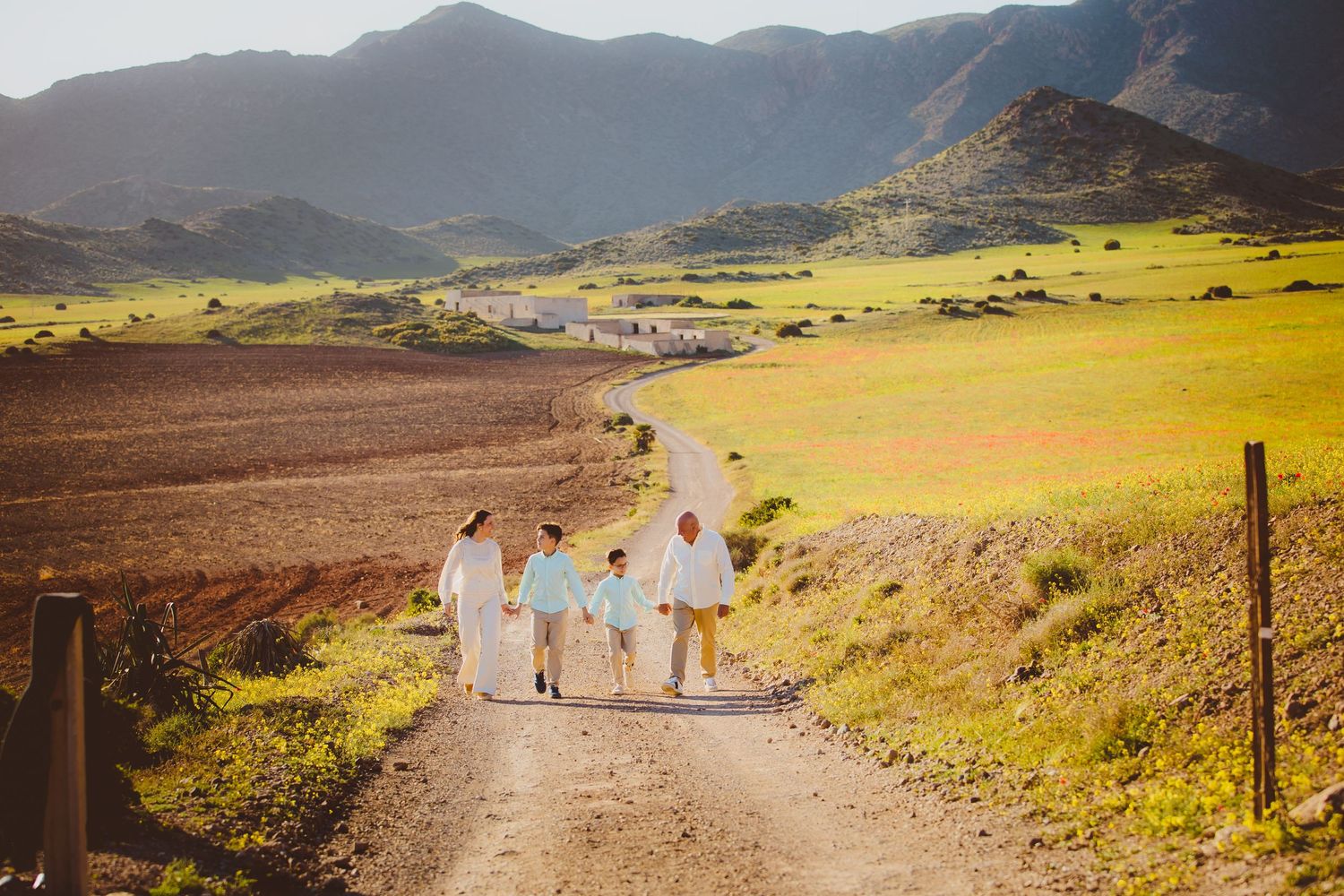 Familia agarrada de la mano en la sesión de comunión de exteriores paseando por los prados de Genoveses en Cabo con las montañas de fondo.