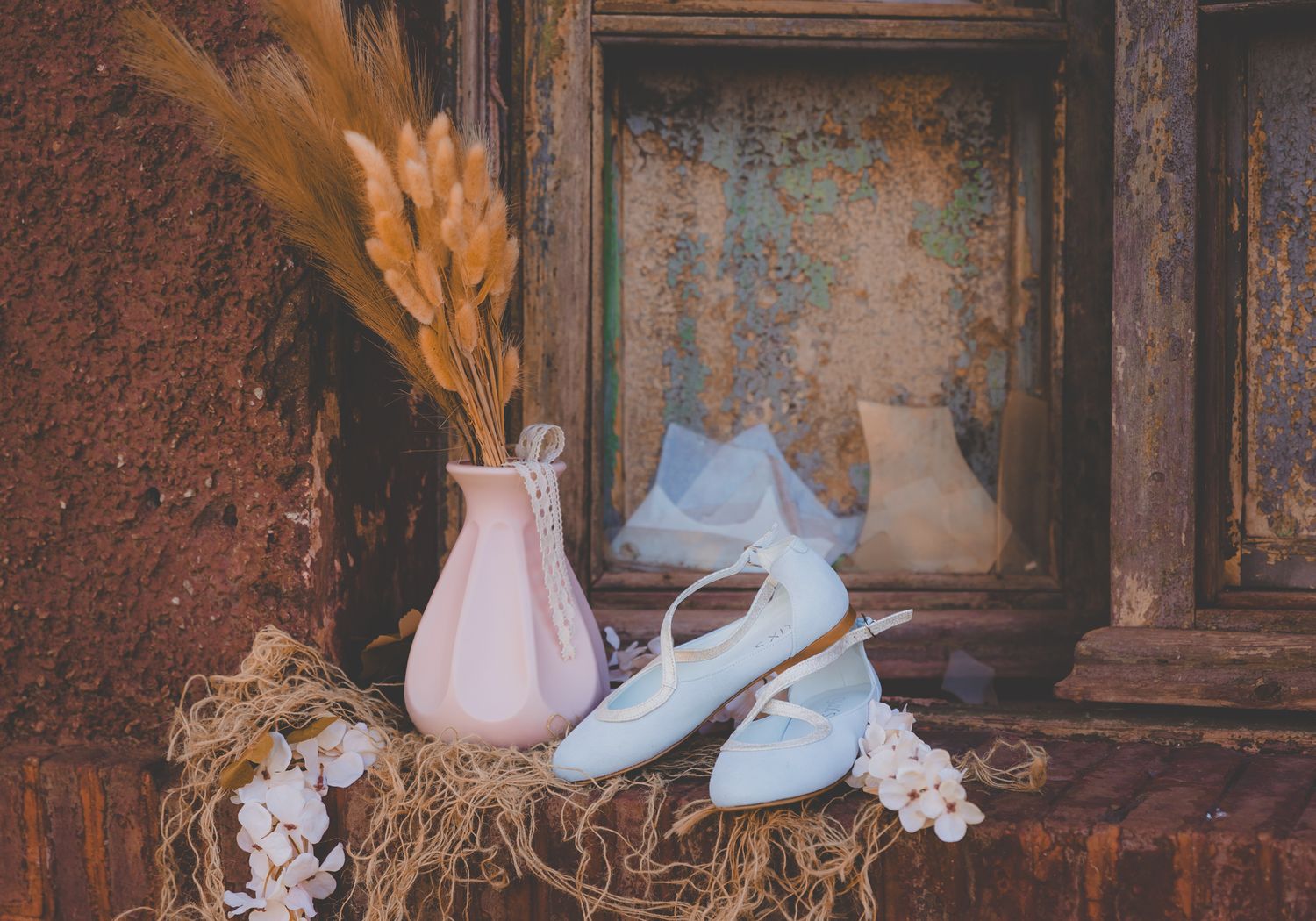 Imagen vintage con zapatillas de ballet azul claro, de comunión, jarrón rosa con trigo seco y marco de madera rústica.