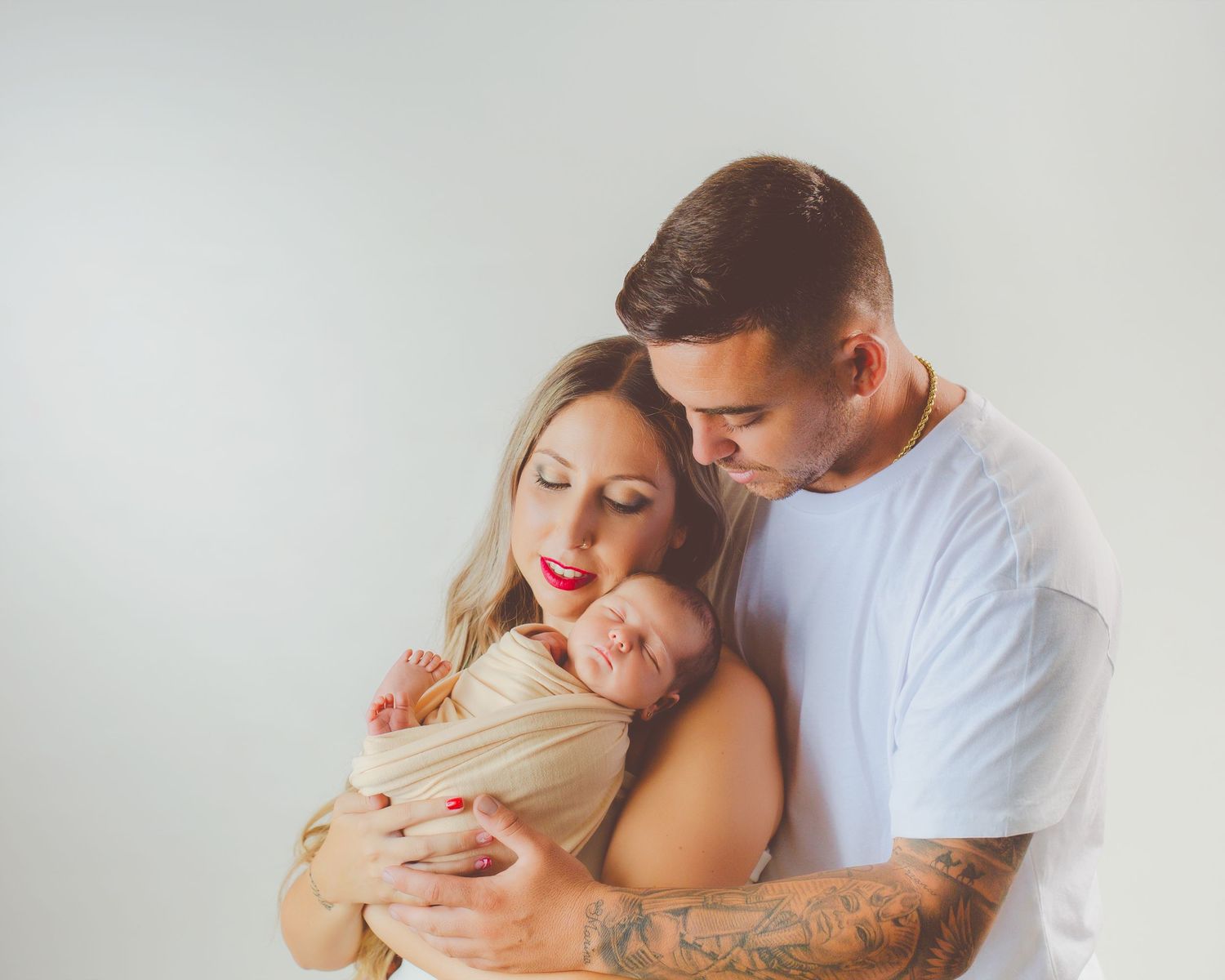 Unos padres sostienen con ternura a su bebé recién nacido dormido, envuelto en una manta beige, en su sesión de estudio en Almería.